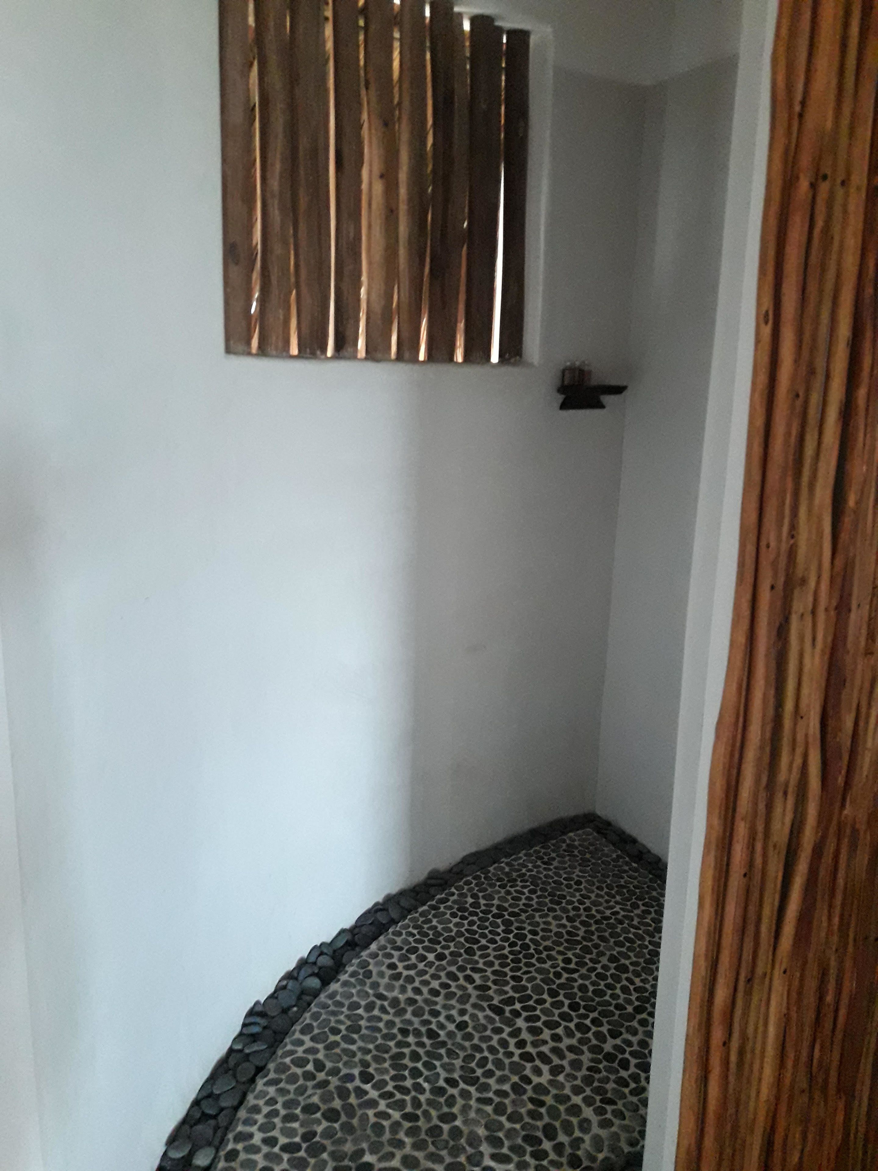 Un área de ducha pequeña y cerrada, con suelo de baldosas y separador de listones de madera.