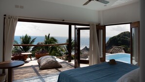 A bedroom with a bed, a ceiling fan, and a view of the ocean and palm trees. - El Alquimista Yoga & Spa (San Pedro Pochutla)