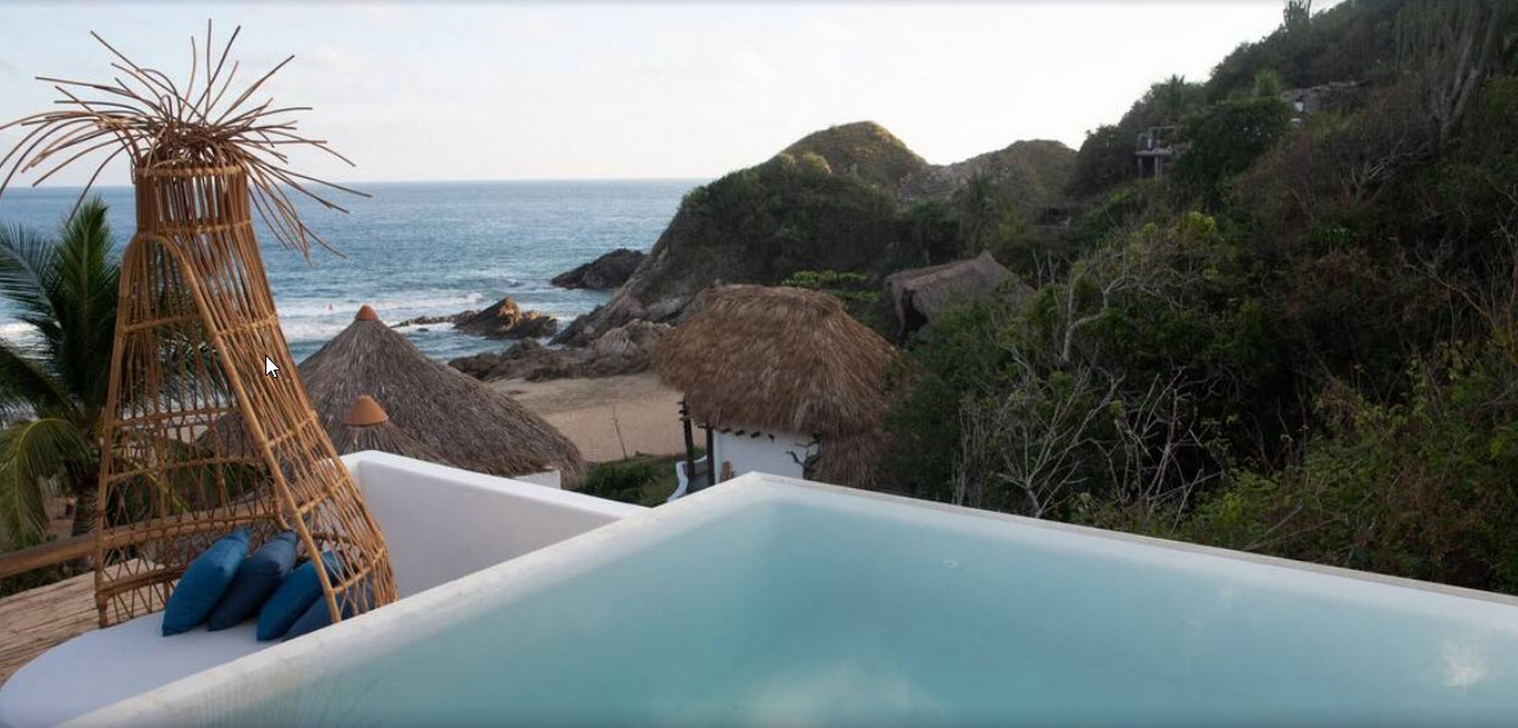 A pool with a view of the ocean and thatched-roof huts.