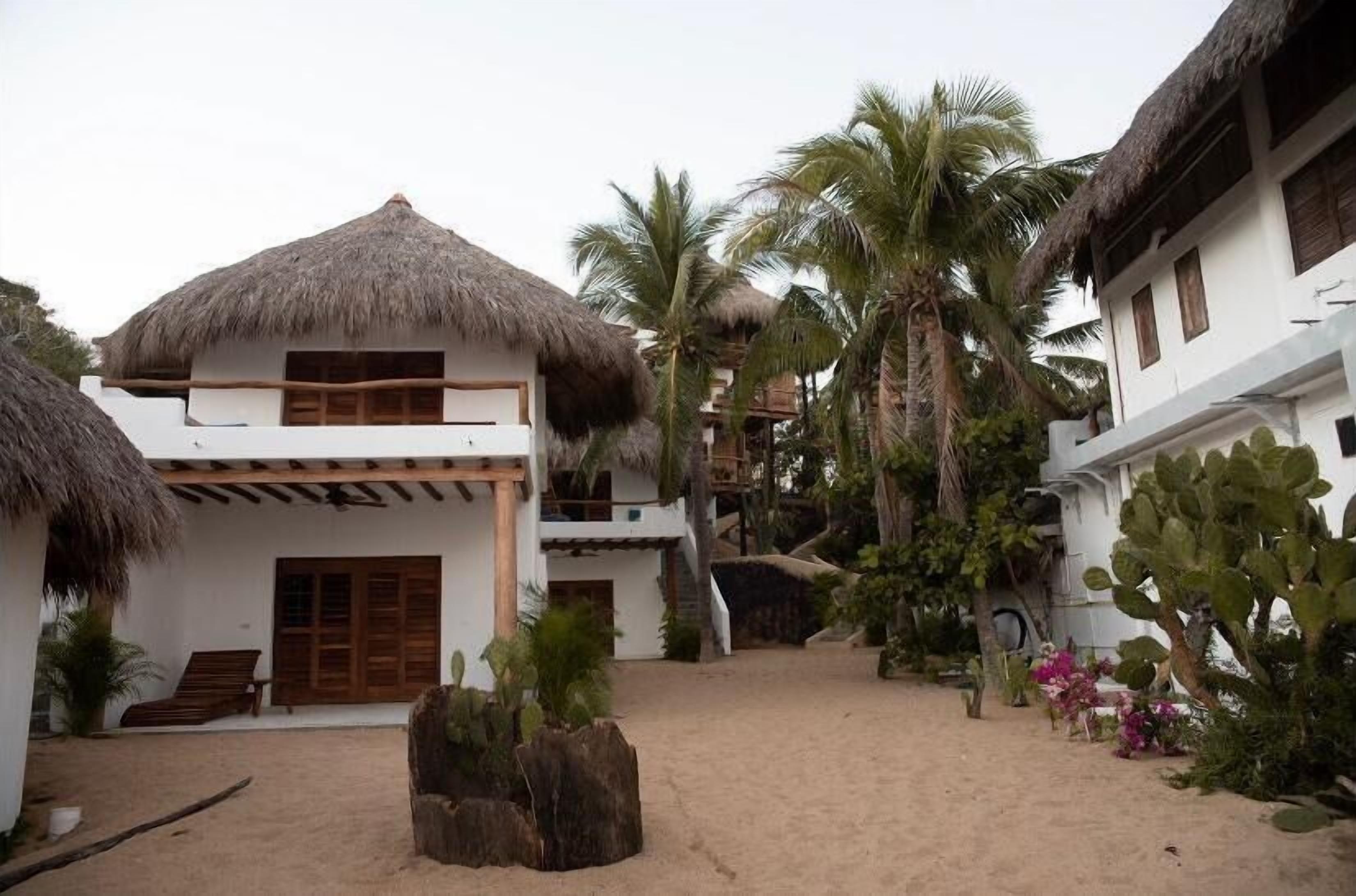 A resort with thatched-roof buildings, palm trees, and a sandy courtyard.