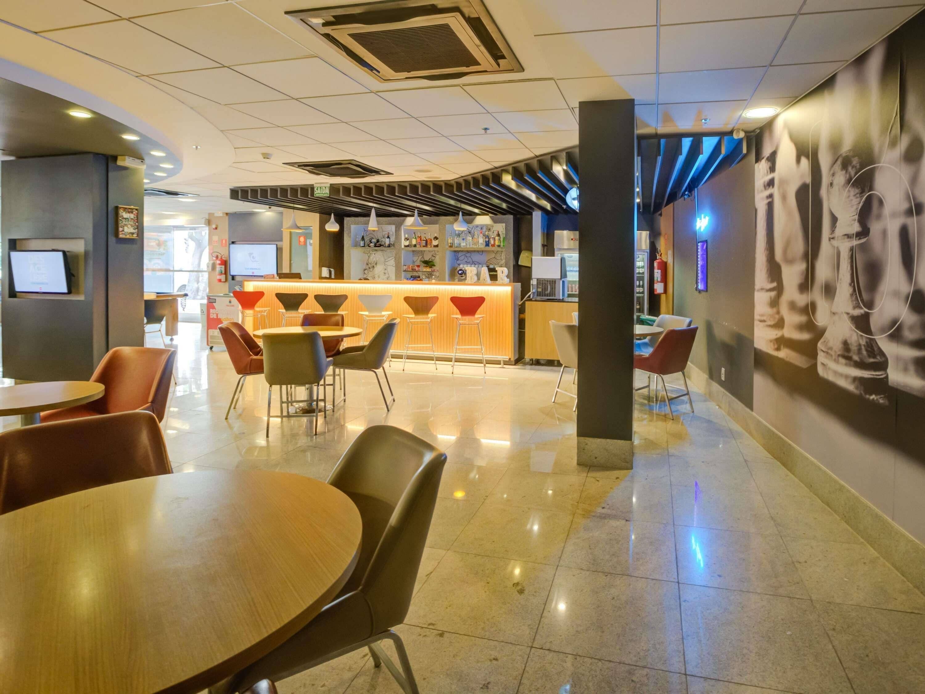 A modern hotel lobby with a bar area, seating arrangements, and a large wall mural.