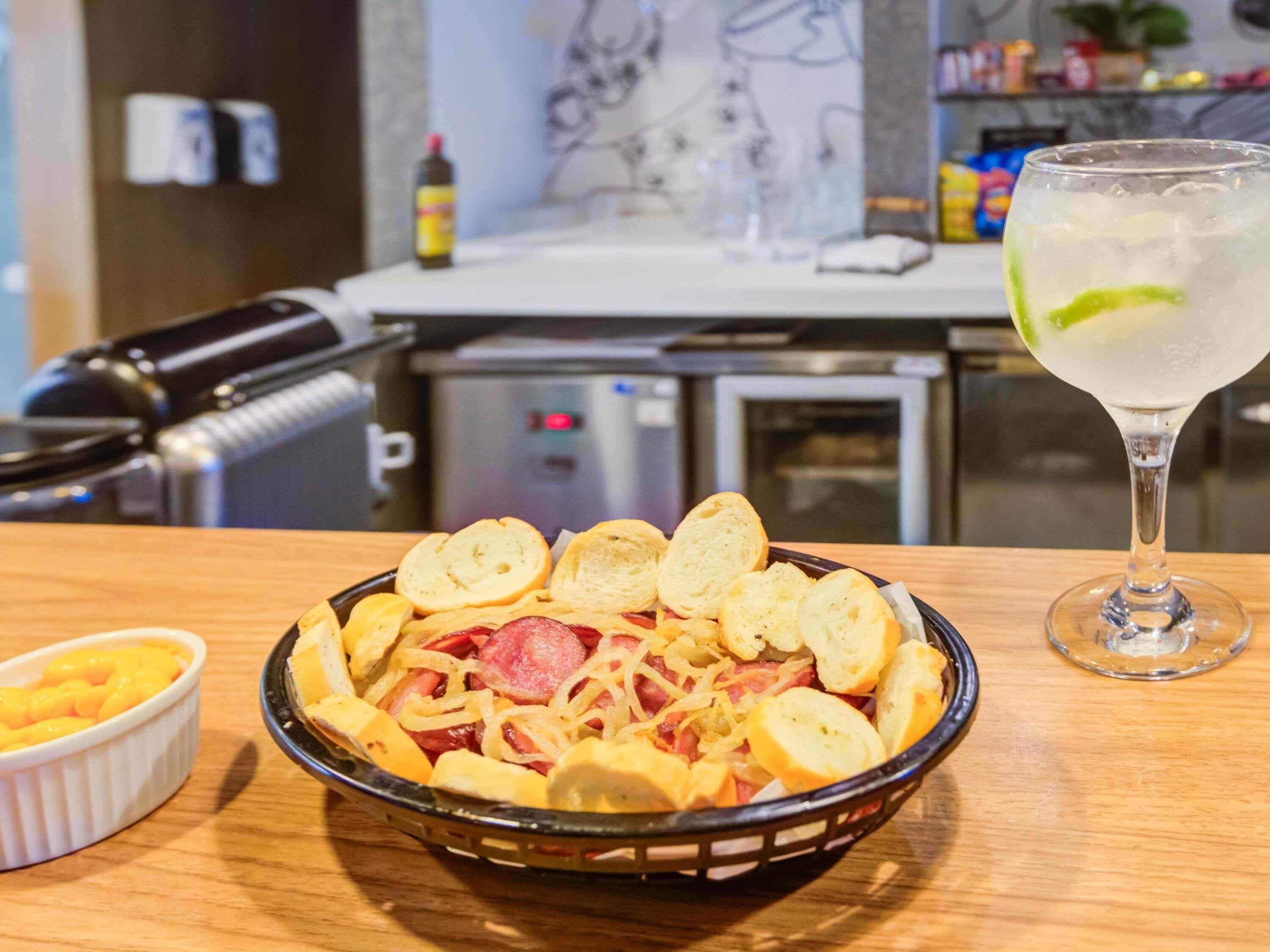 A bowl of food with bread, sausage, and cheese, and a glass of a clear beverage with a lime slice on a table.