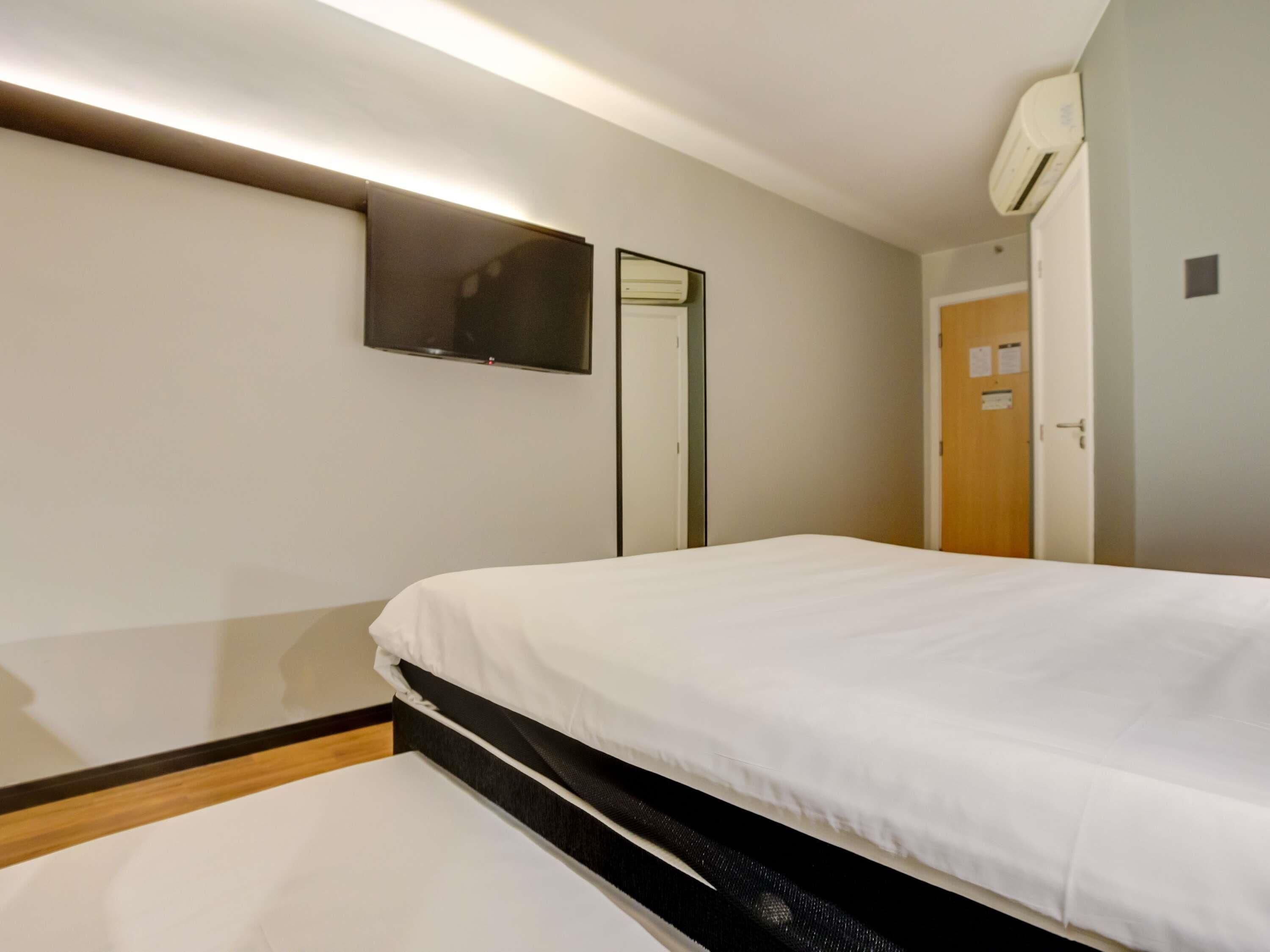 Habitación de hotel con cama, televisor de pantalla plana en la pared, una puerta y equipo de aire acondicionado.