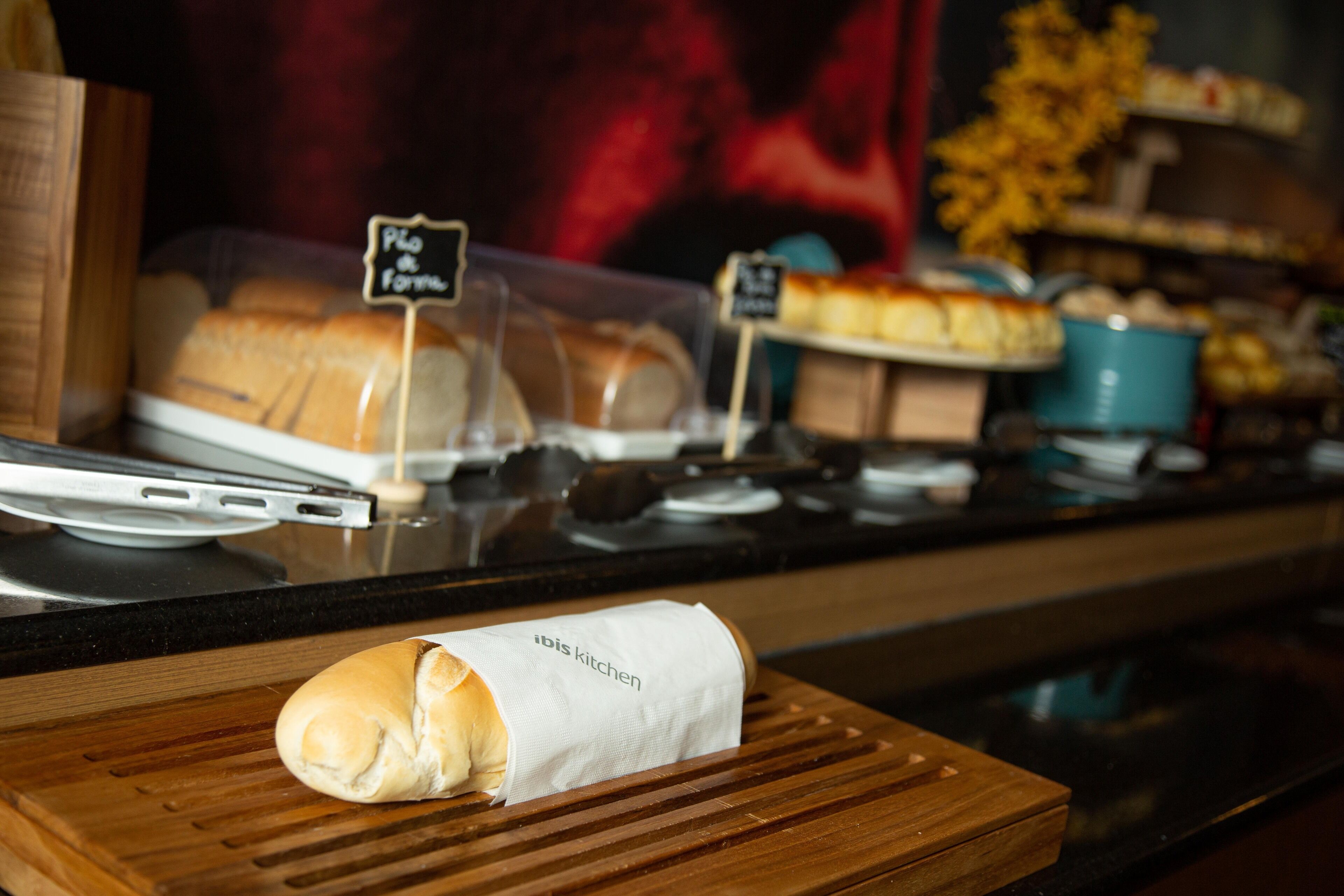 A bakery display with various breads and pastries, including a loaf labeled "Pão de Farinha".