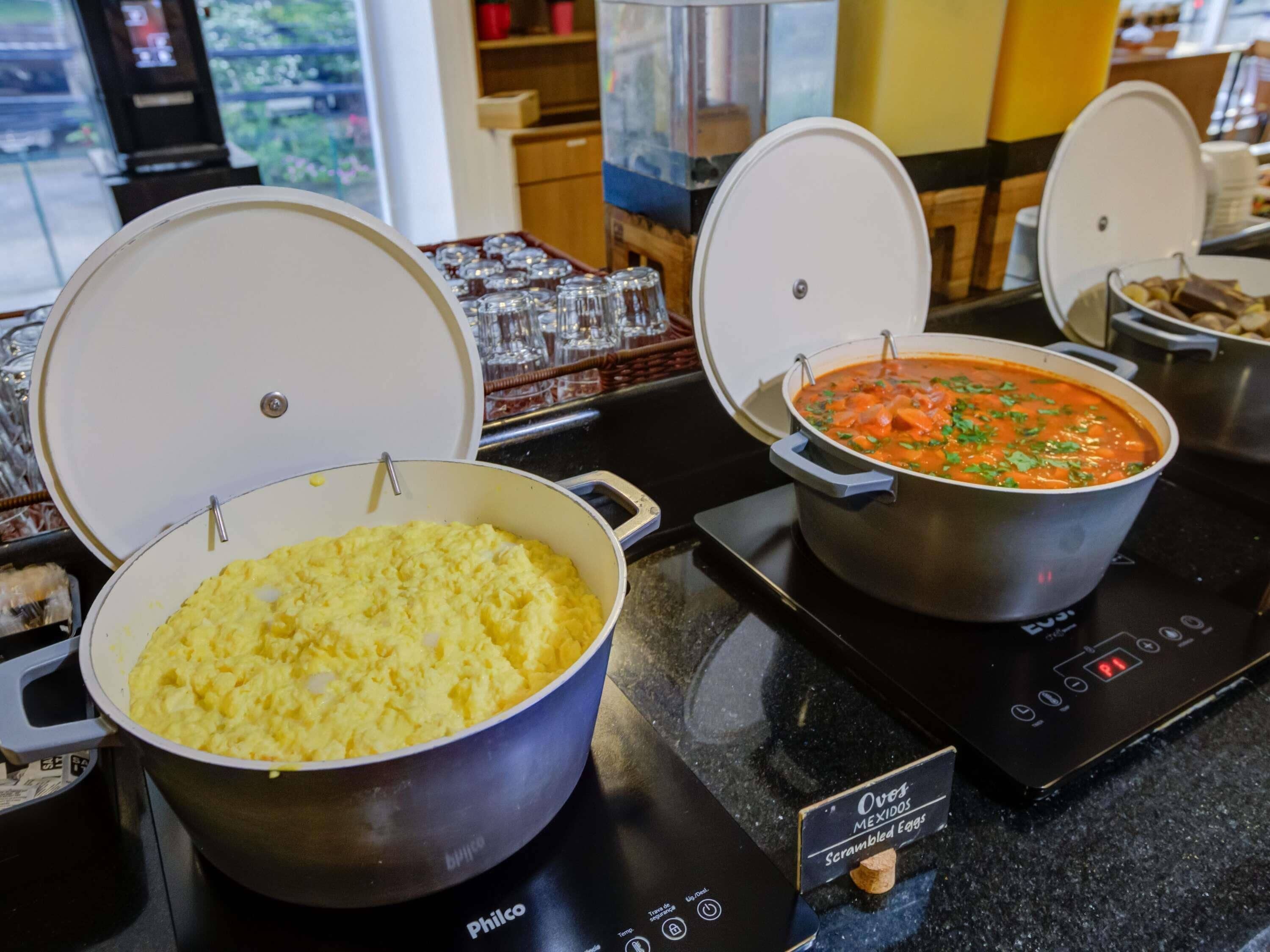 Two pots of food on a black induction cooktop, one with scrambled eggs and the other with a tomato-based dish, with a label indicating 'Over Easy Scrambled Eggs'.