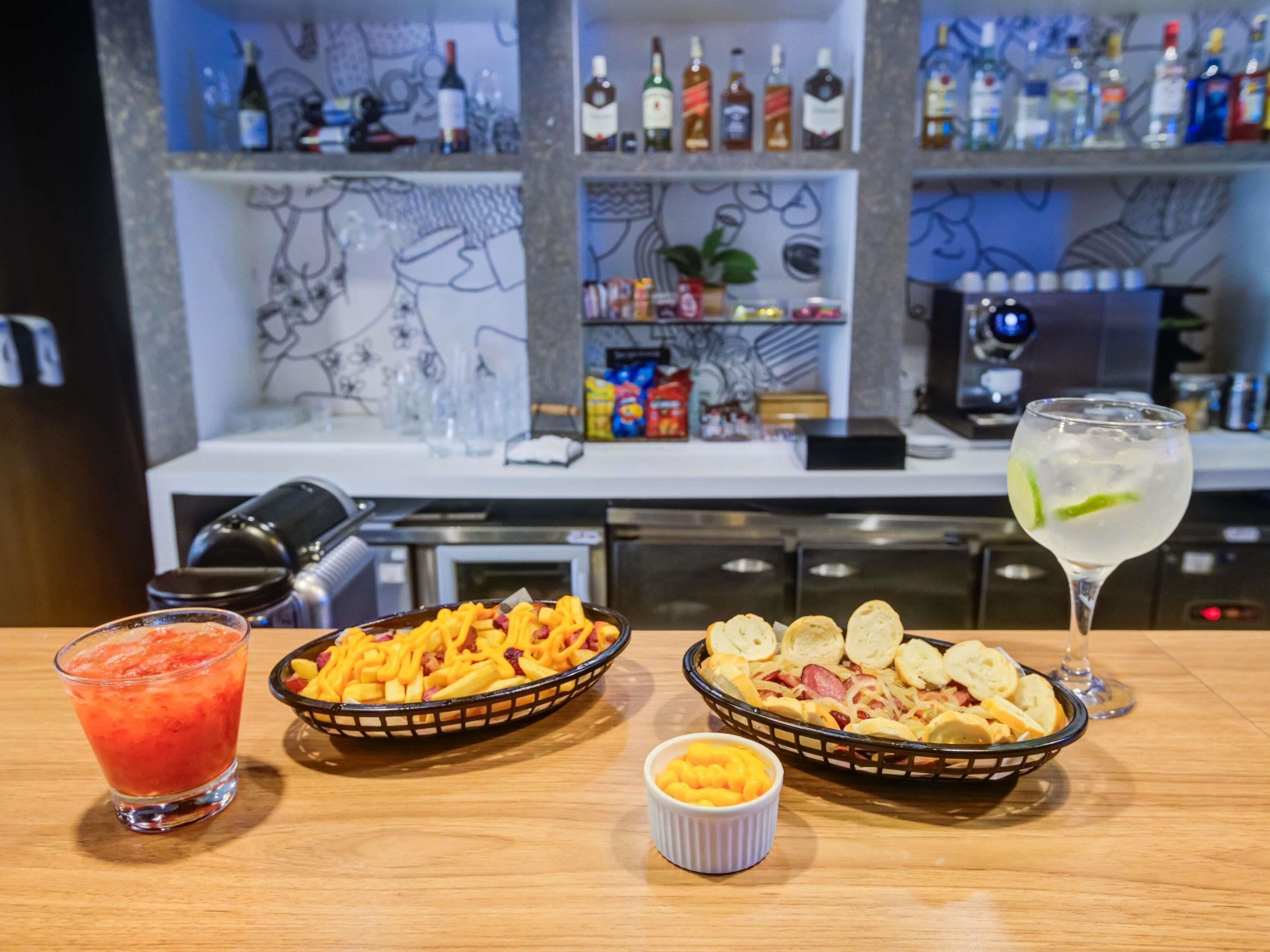 A bar area with a variety of bottles and glasses, a bowl of nachos, a glass of red drink, and a glass of clear drink with lime.