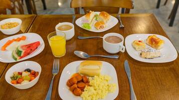 Una mesa de comedor con platos de comida, un vaso de jugo de naranja y una taza de café.