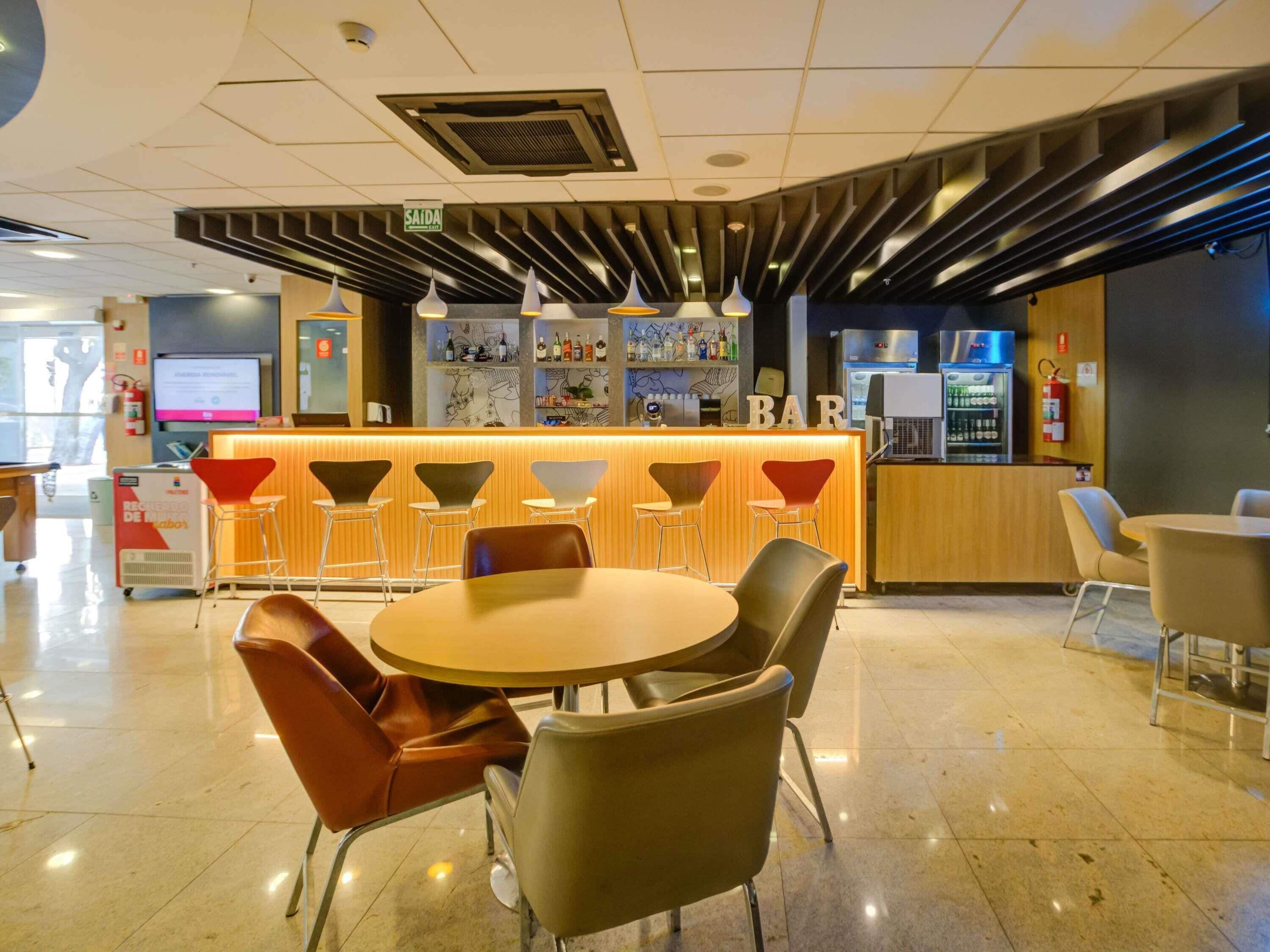 Zona de bar moderna con mostrador, taburetes y una mesa redonda con sillas.