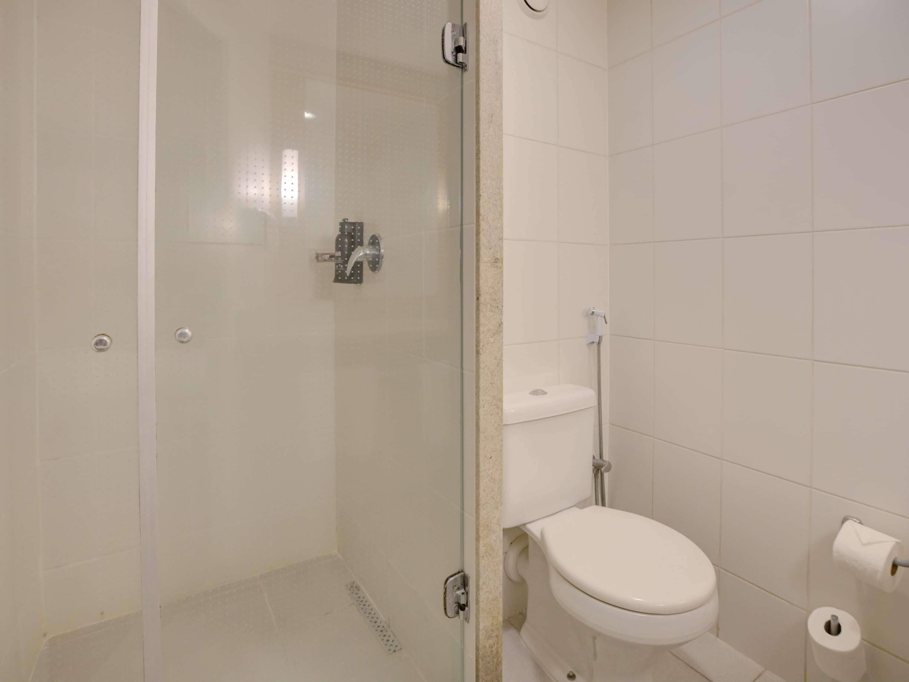 Un baño con ducha de mampara de vidrio, inodoro y rollo de papel higiénico.