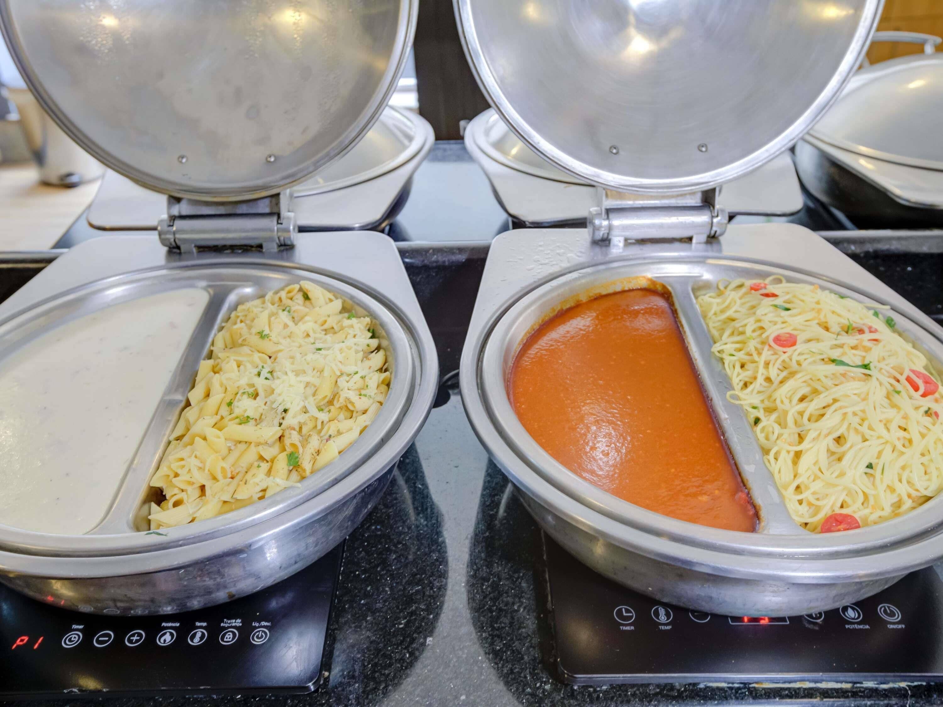 Two electric griddles with pasta dishes, one with a creamy sauce and the other with a tomato-based sauce.