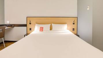 A hotel room with a large bed, a wooden headboard, two bedside tables, a desk with a chair, and a nightstand.