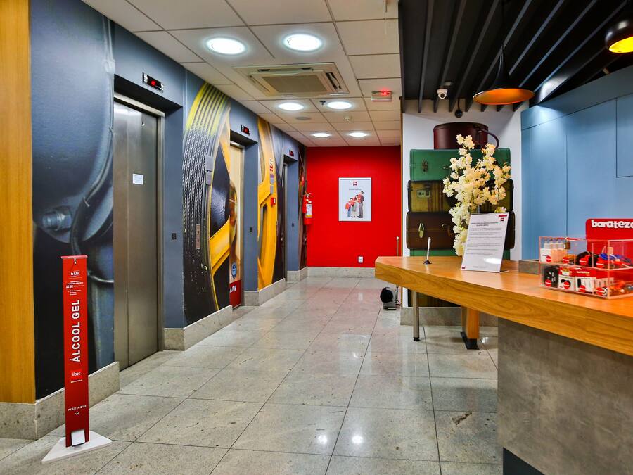 Um saguão de hotel com balcão de recepção, uma parede vermelha e um elevador.