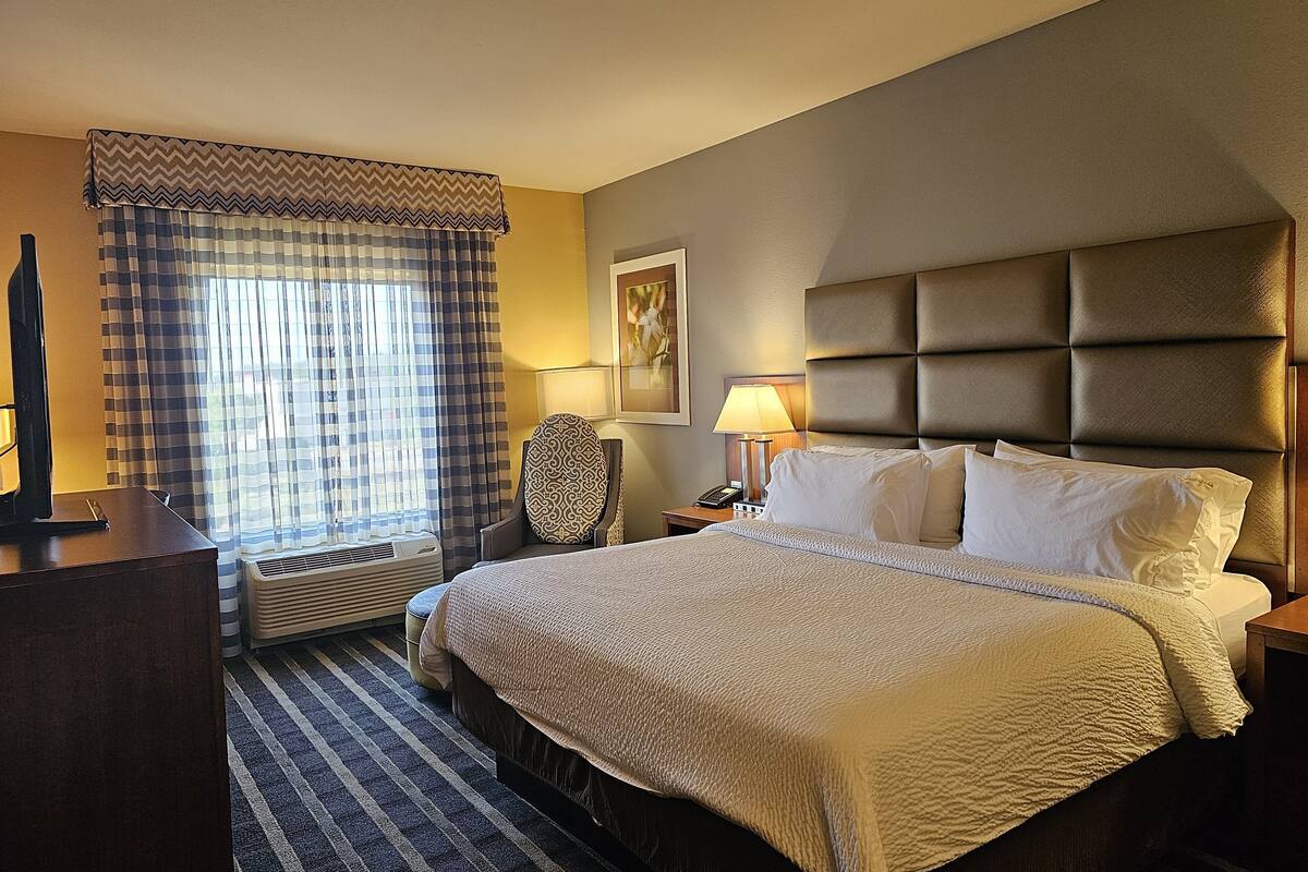 A hotel room with a large bed, a desk, a chair, a lamp, and a window with curtains.