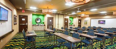 A conference room with multiple tables and chairs, a large screen, and a patterned carpet.