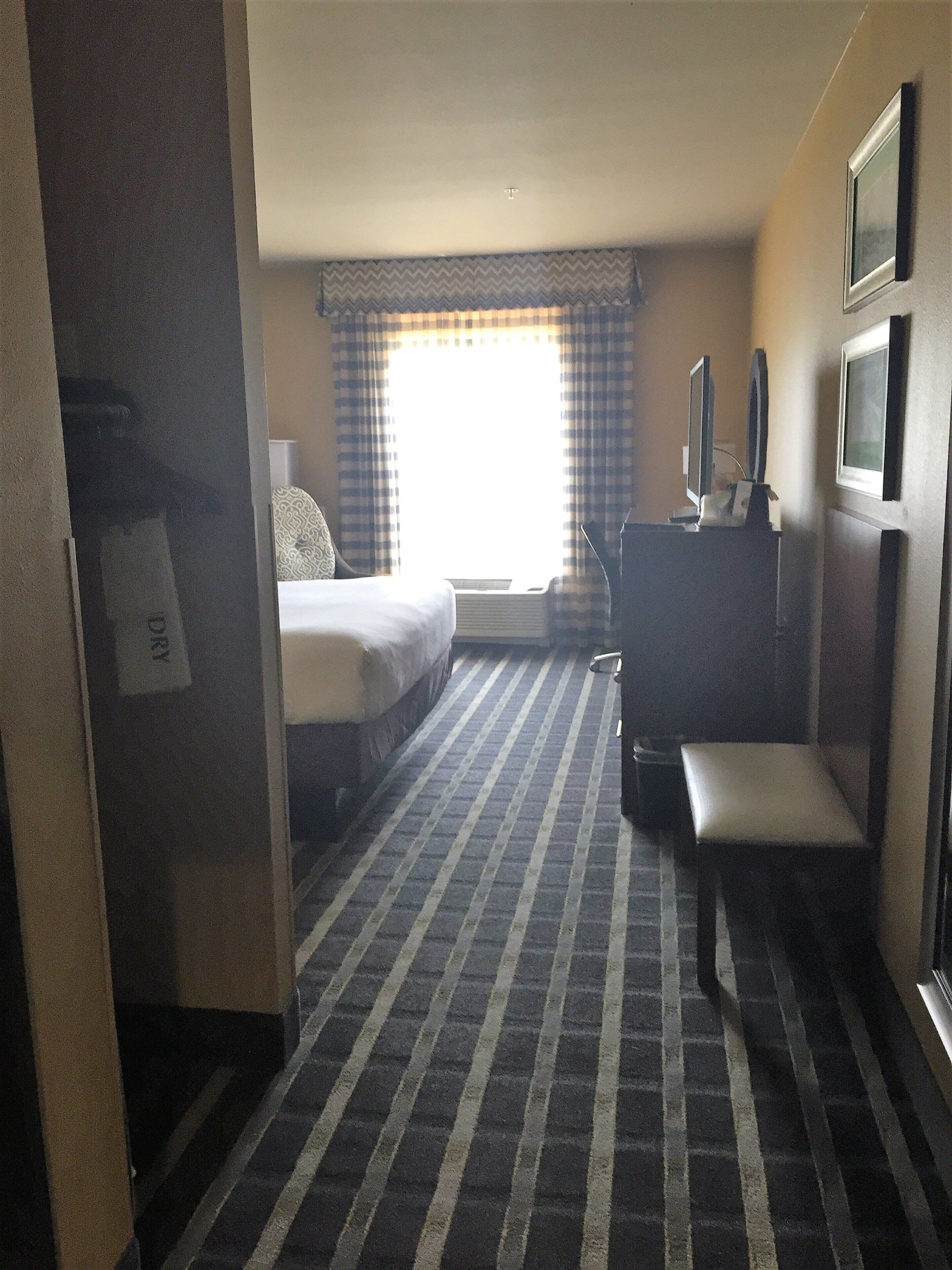 A hotel room with a bed, a desk, a chair, a television, and a window with curtains.
