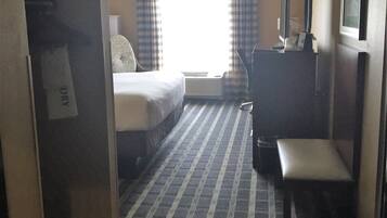 A hotel room with a bed, a desk, a chair, a television, and a window with curtains.