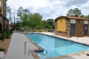 A swimming pool with a stone and brick pool deck, a small covered area, and a fenced patio with chairs.