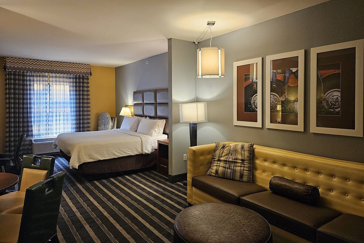 A hotel room with a bed, a sofa, a chair, a table, and a window with curtains.