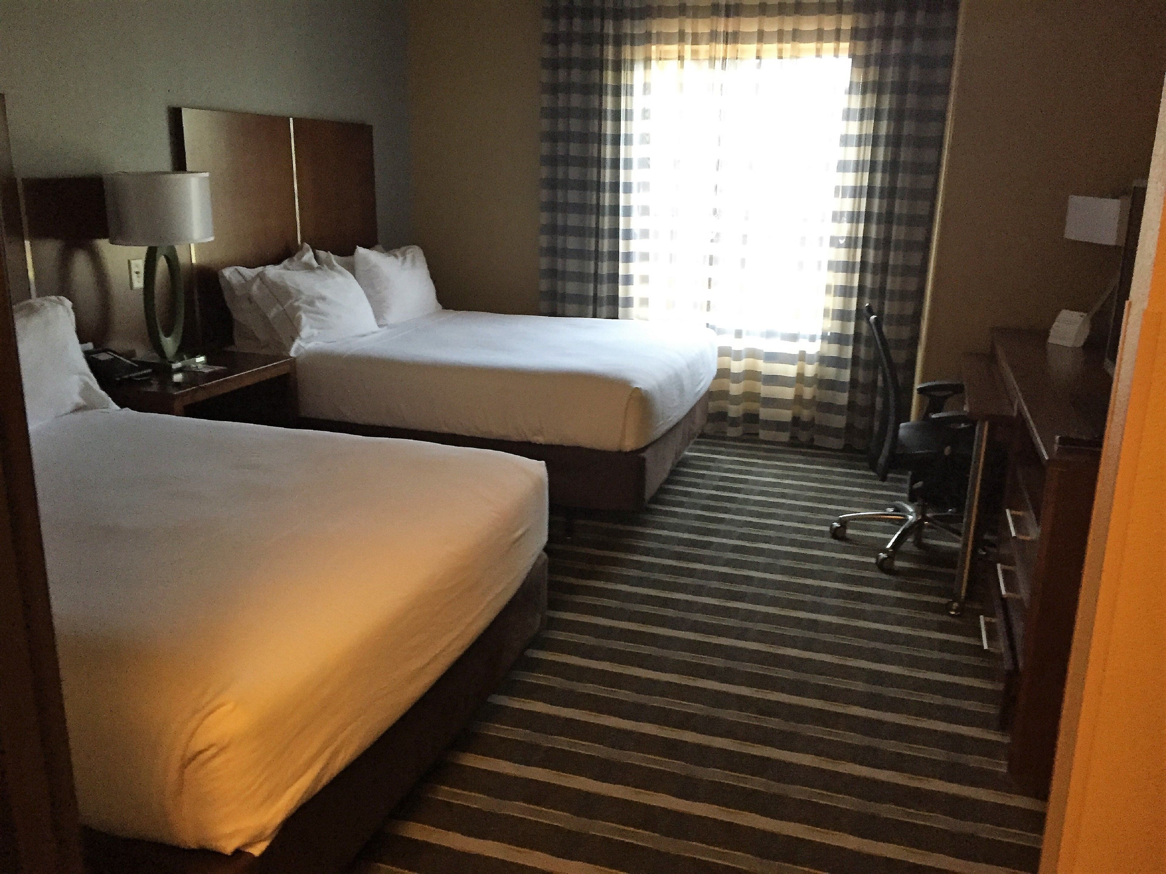 A hotel room with two beds, a desk, a chair, and a window with curtains.