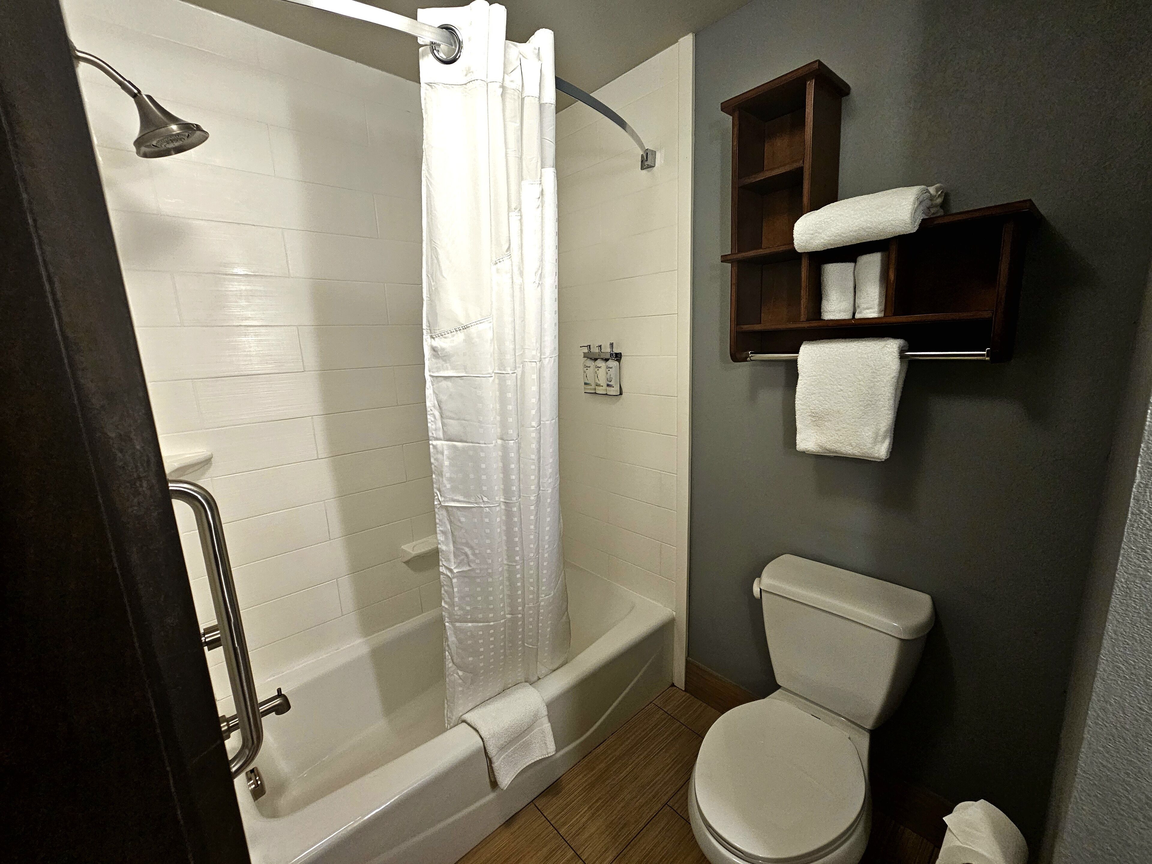 A bathroom with a shower, toilet, and a shelf with towels.
