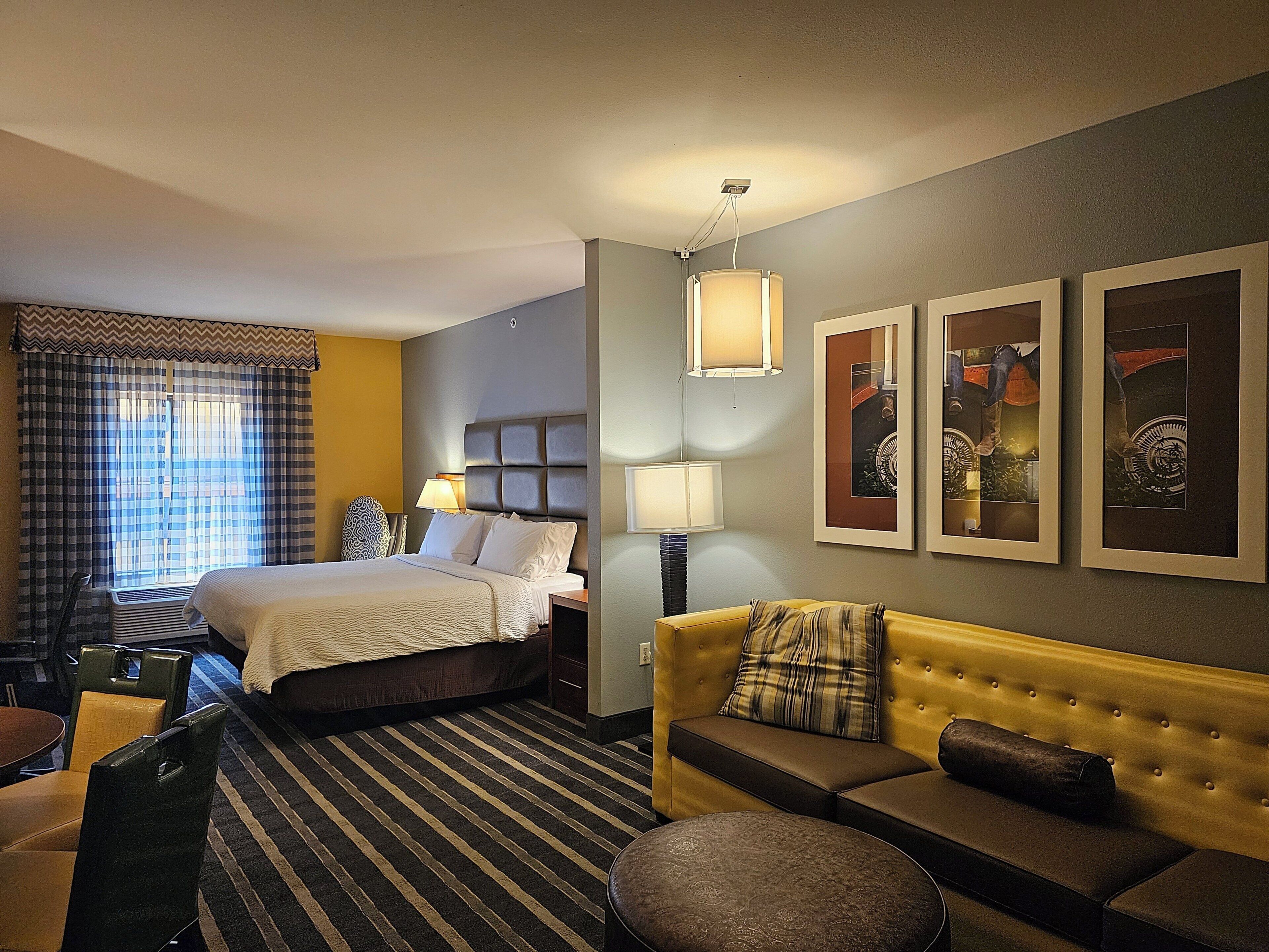 Una habitación de hotel con una cama, un sofá, una silla, una lámpara y obras de arte en la pared.