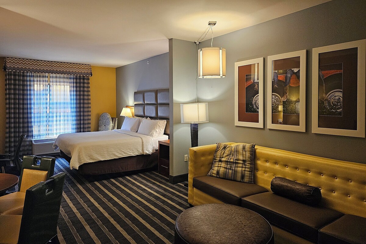A hotel room with a bed, a sofa, a chair, a table, and a window with curtains.