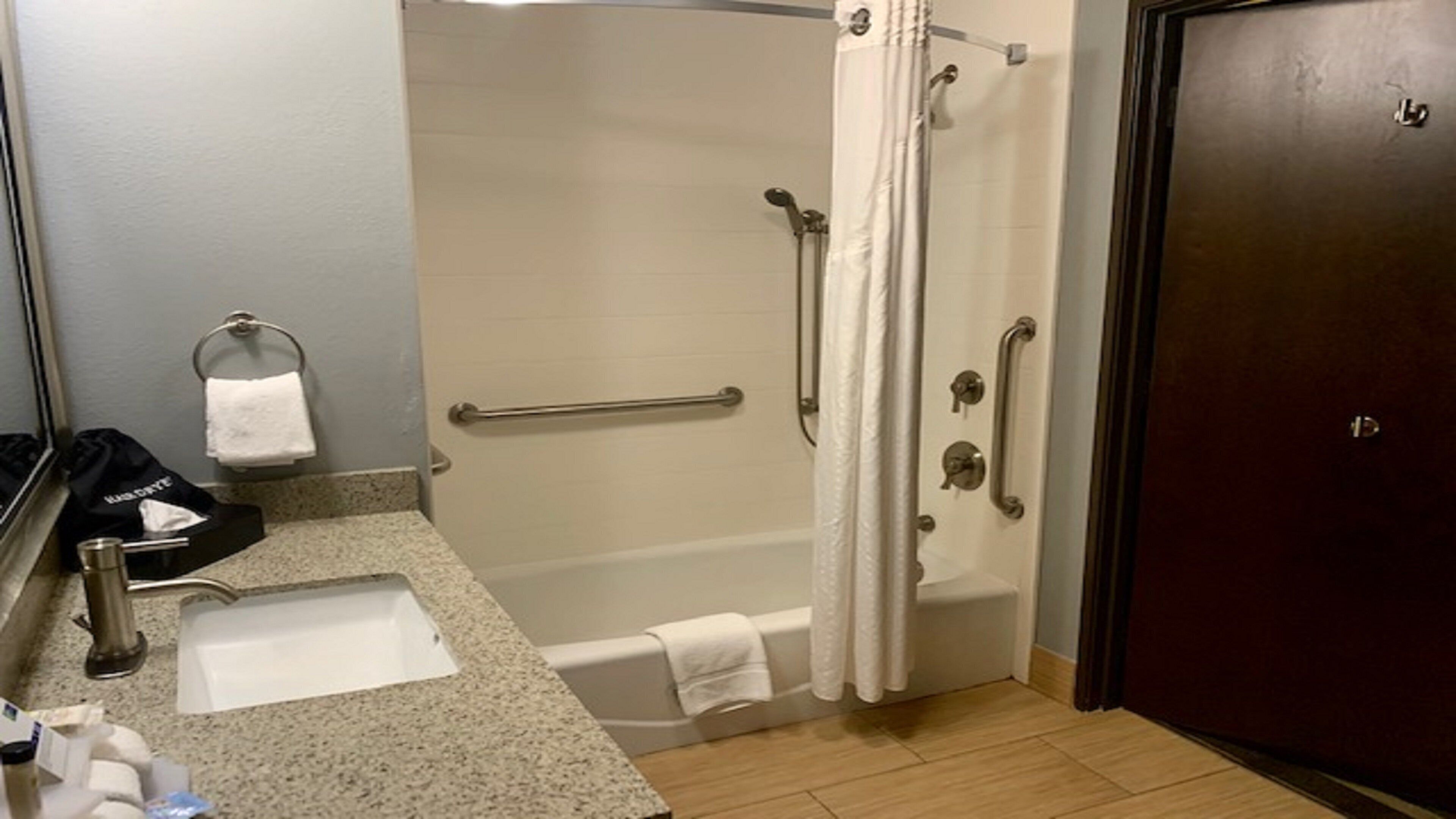 A bathroom with a shower, grab bars, a towel rack, and a sink.