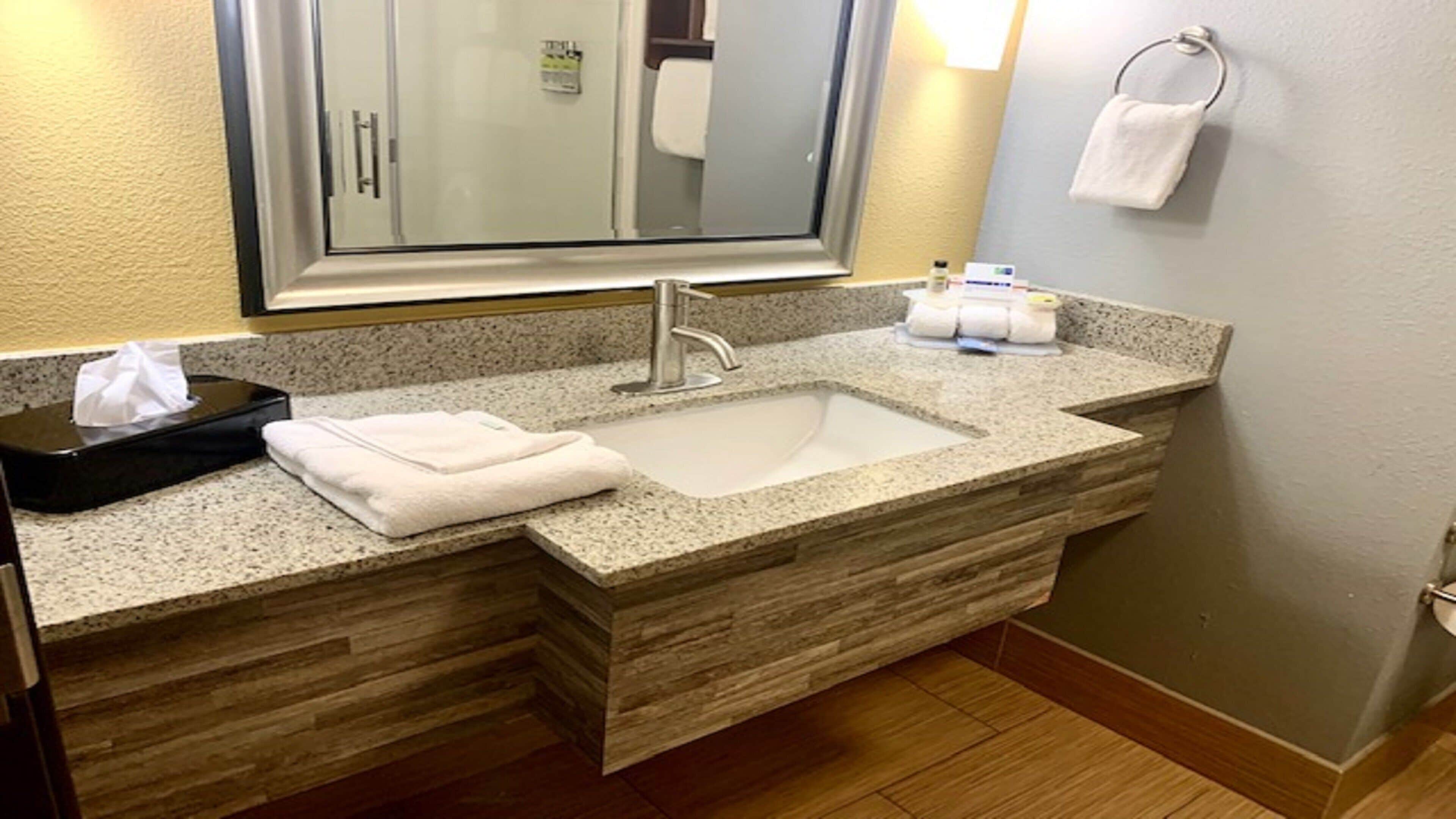 A bathroom with a granite countertop, a sink, a towel rack, and a mirror.