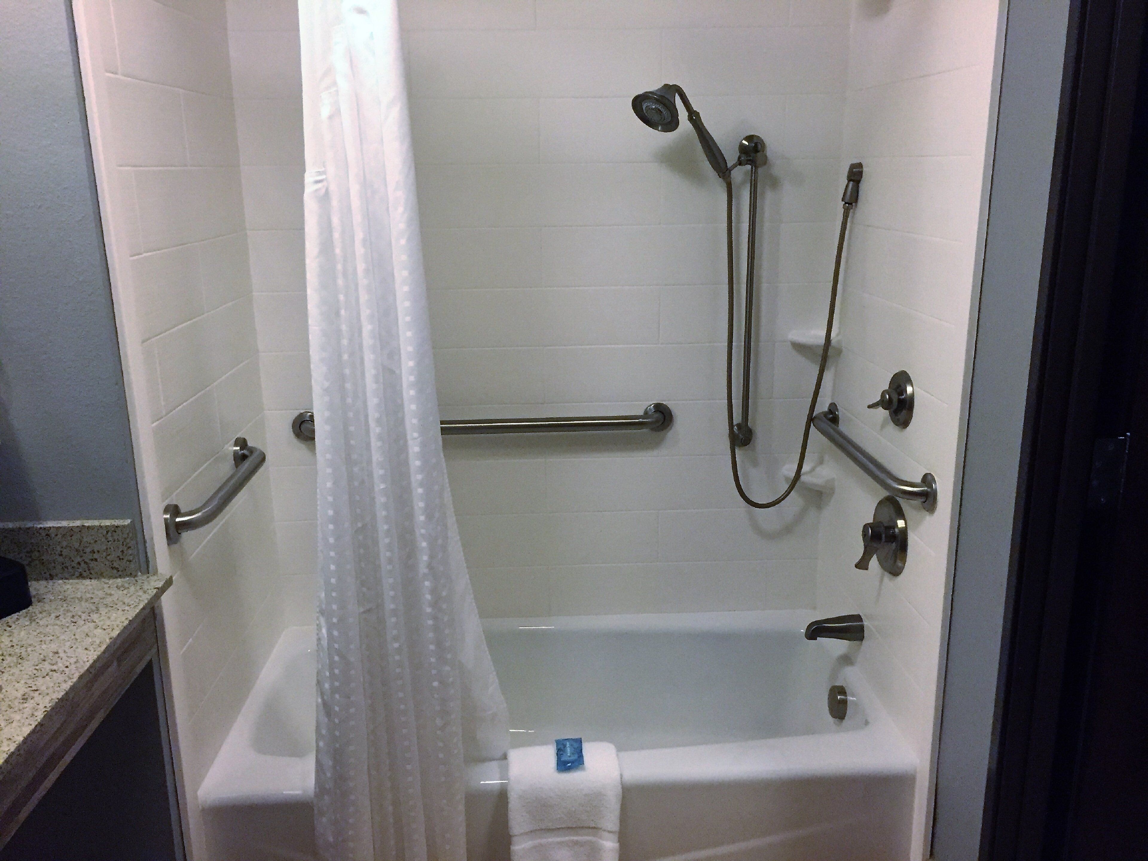 A walk-in shower with a glass door, grab bars, a handheld showerhead, and a towel rack.