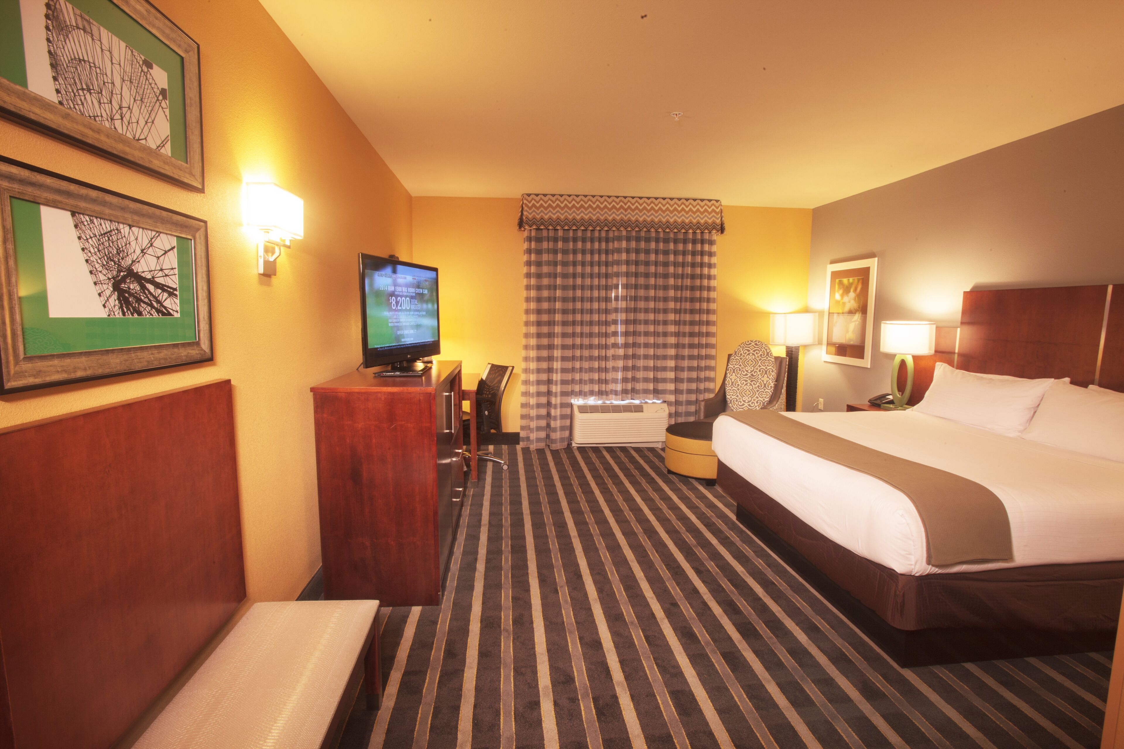 A hotel room with a bed, a desk with a computer, a television, and a window with curtains.