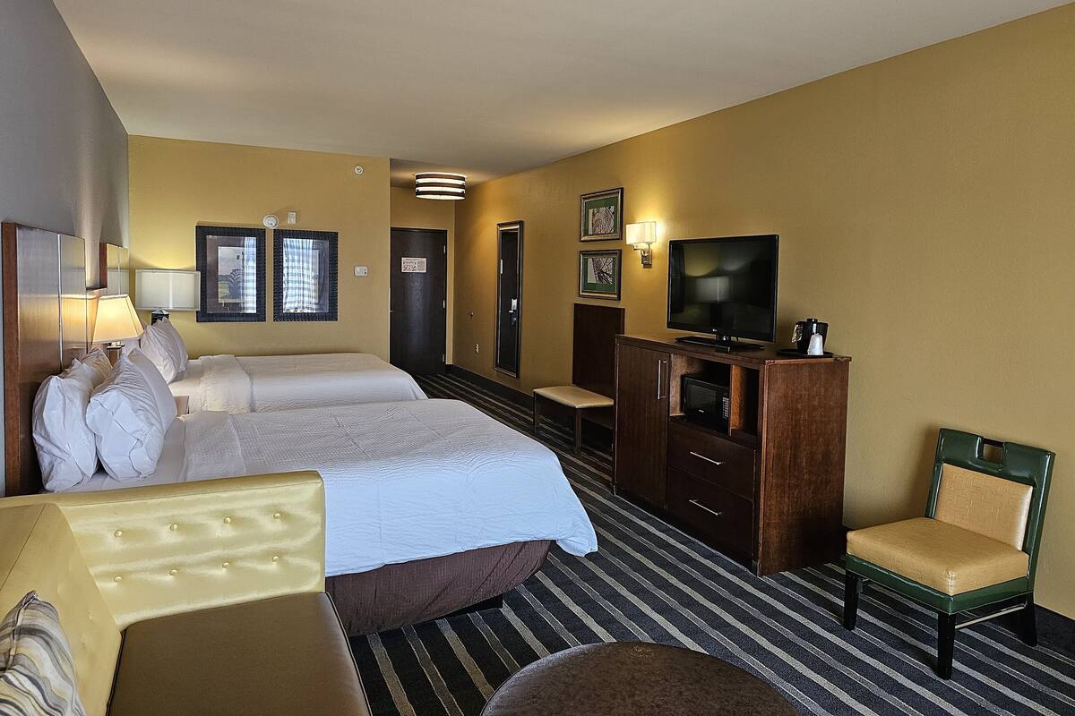 A hotel room with two beds, a television, a desk, and a chair.