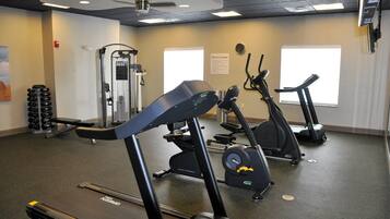 A fitness center with exercise equipment, a wall clock, and a sign indicating the location.