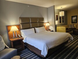 Habitación de hotel con una cama grande, dos mesitas de noche con lámparas, un sofá y una pequeña mesa redonda.