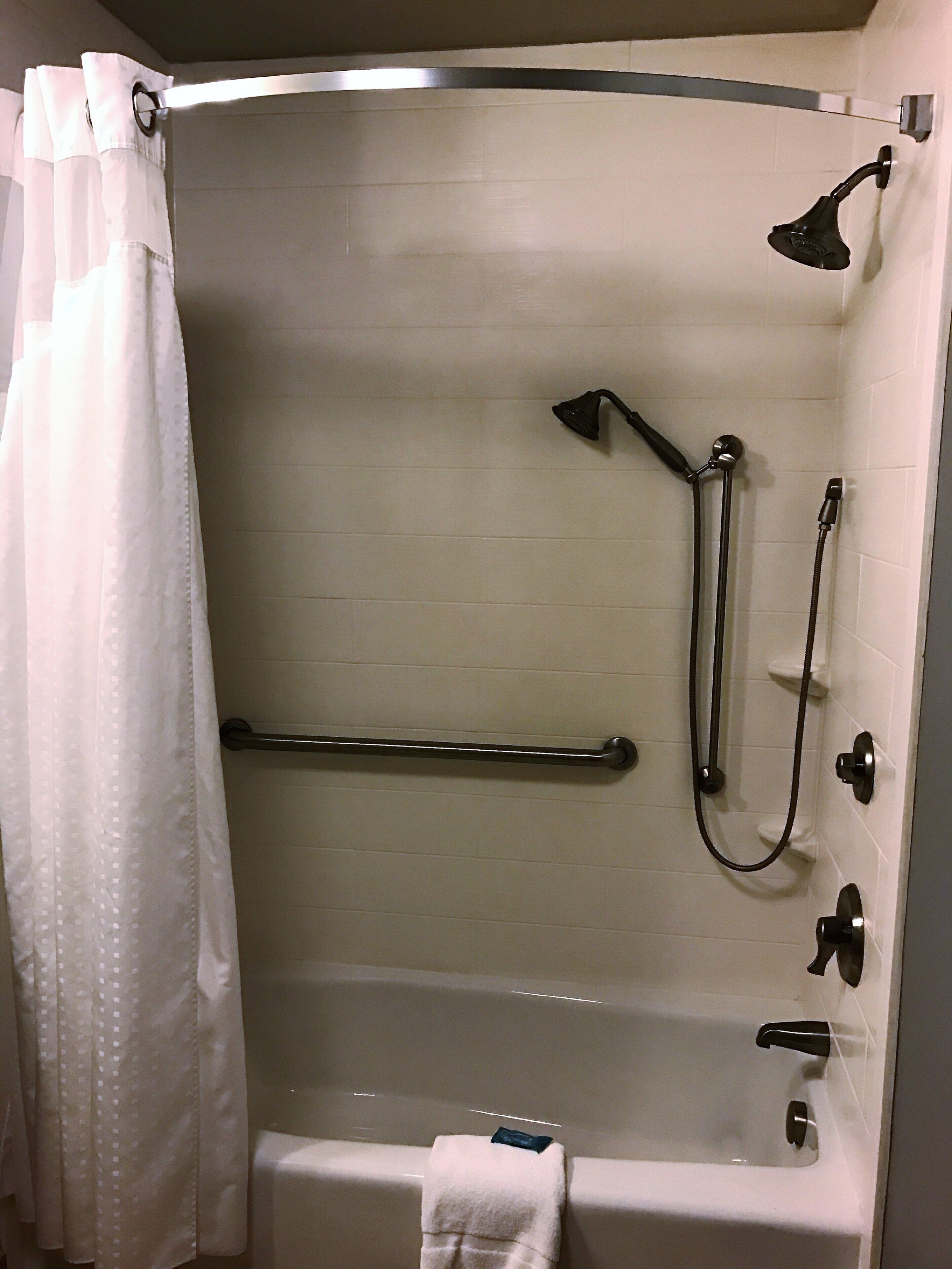 A bathroom with a bathtub, a shower head, a grab bar, and a towel rack.