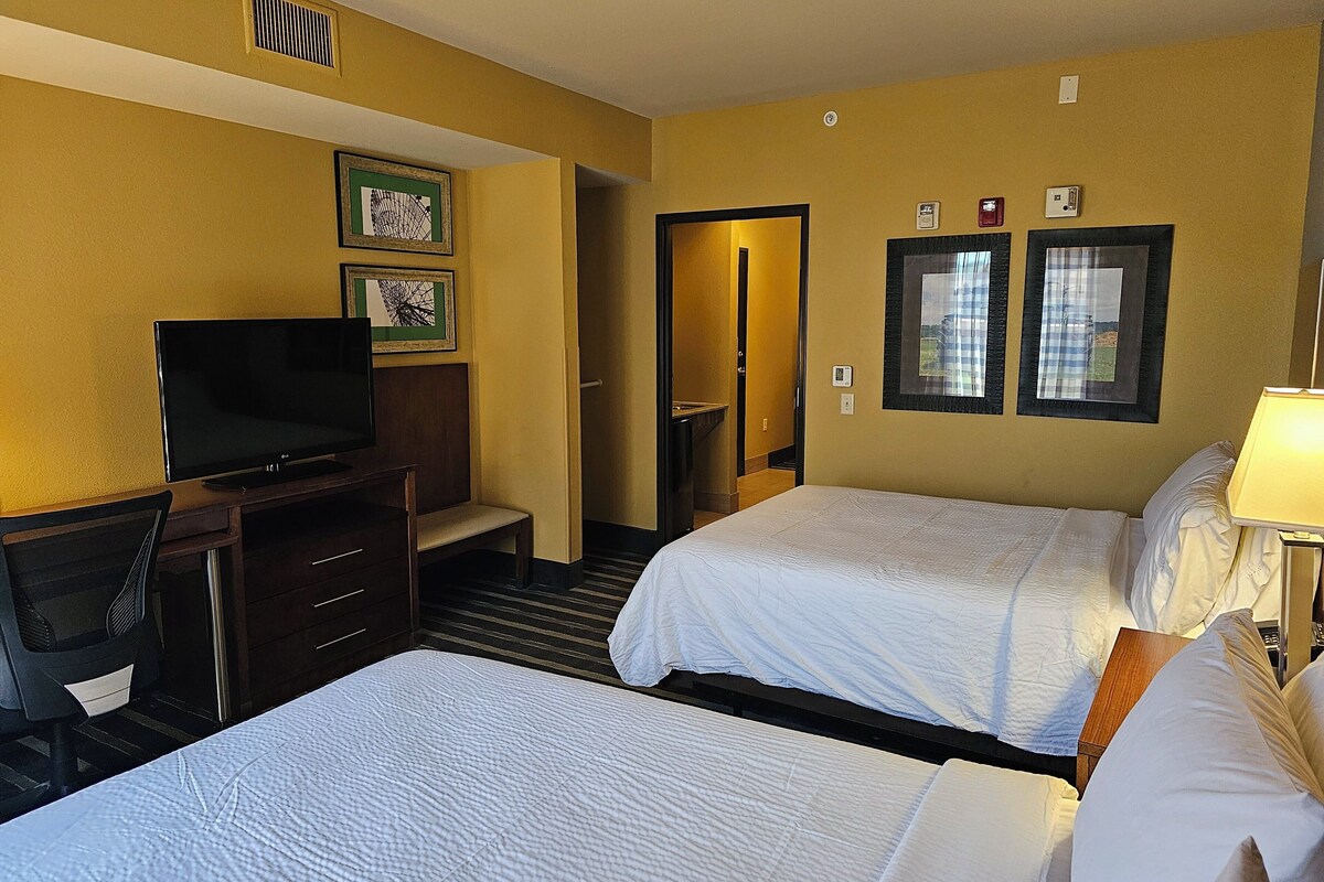 A hotel room with two beds, a TV, a desk, and a mirror.