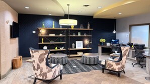 Ein moderner Arbeitsraum mit gewölbter Decke, einem zentralen Bücherregal, zwei Ledersesseln, einem runden Hocker und einem Schreibtisch mit Computer und Drucker.