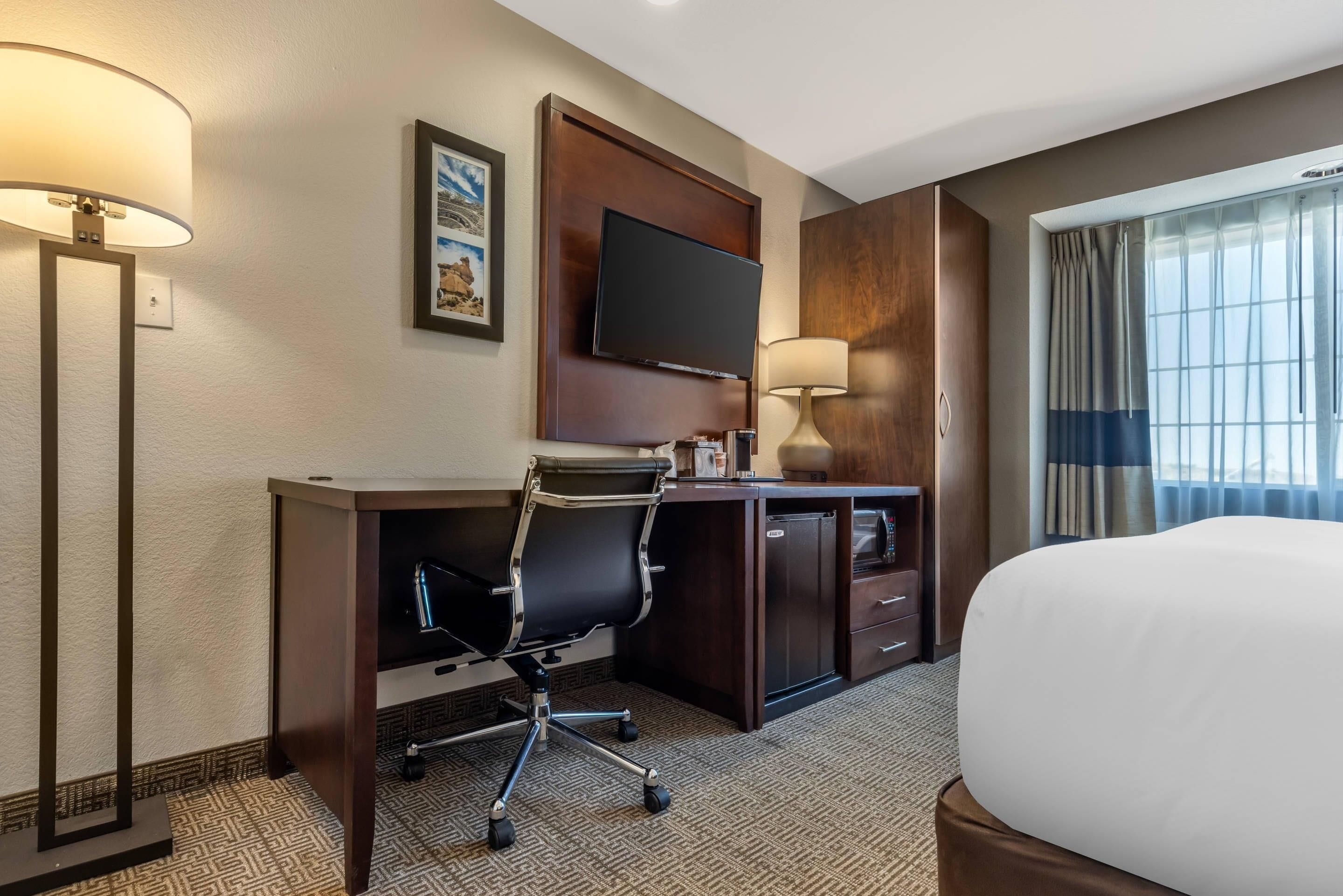 A hotel room with a bed, desk, chair, television, and a window with curtains.