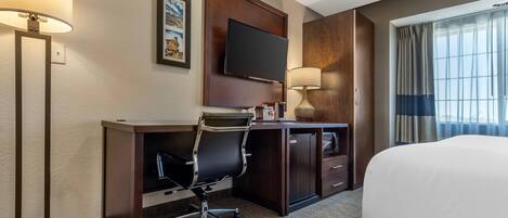 A hotel room with a bed, desk, chair, television, and a window with curtains.
