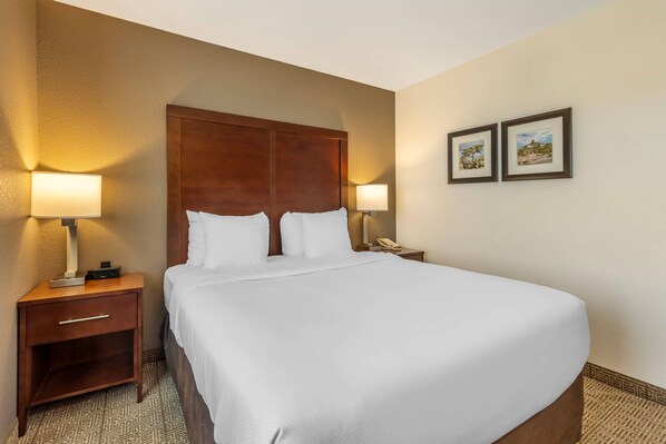 A neatly made bed with white linens, a wooden headboard, and two bedside lamps.