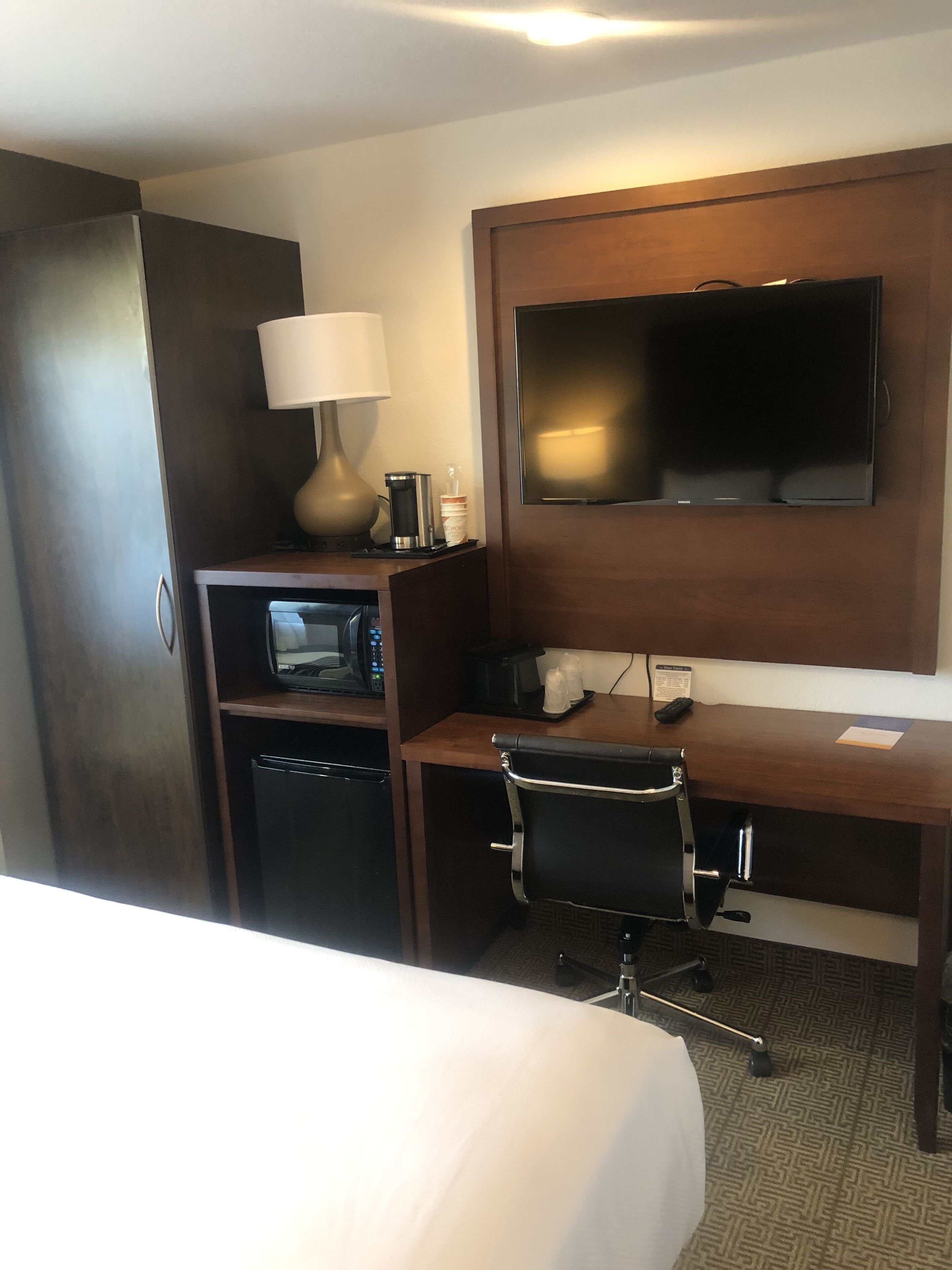 A hotel room with a bed, a desk with a chair, a television, a microwave, and a coffee maker.