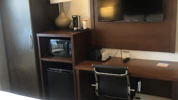 A hotel room with a bed, a desk with a chair, a television, a microwave, and a coffee maker.