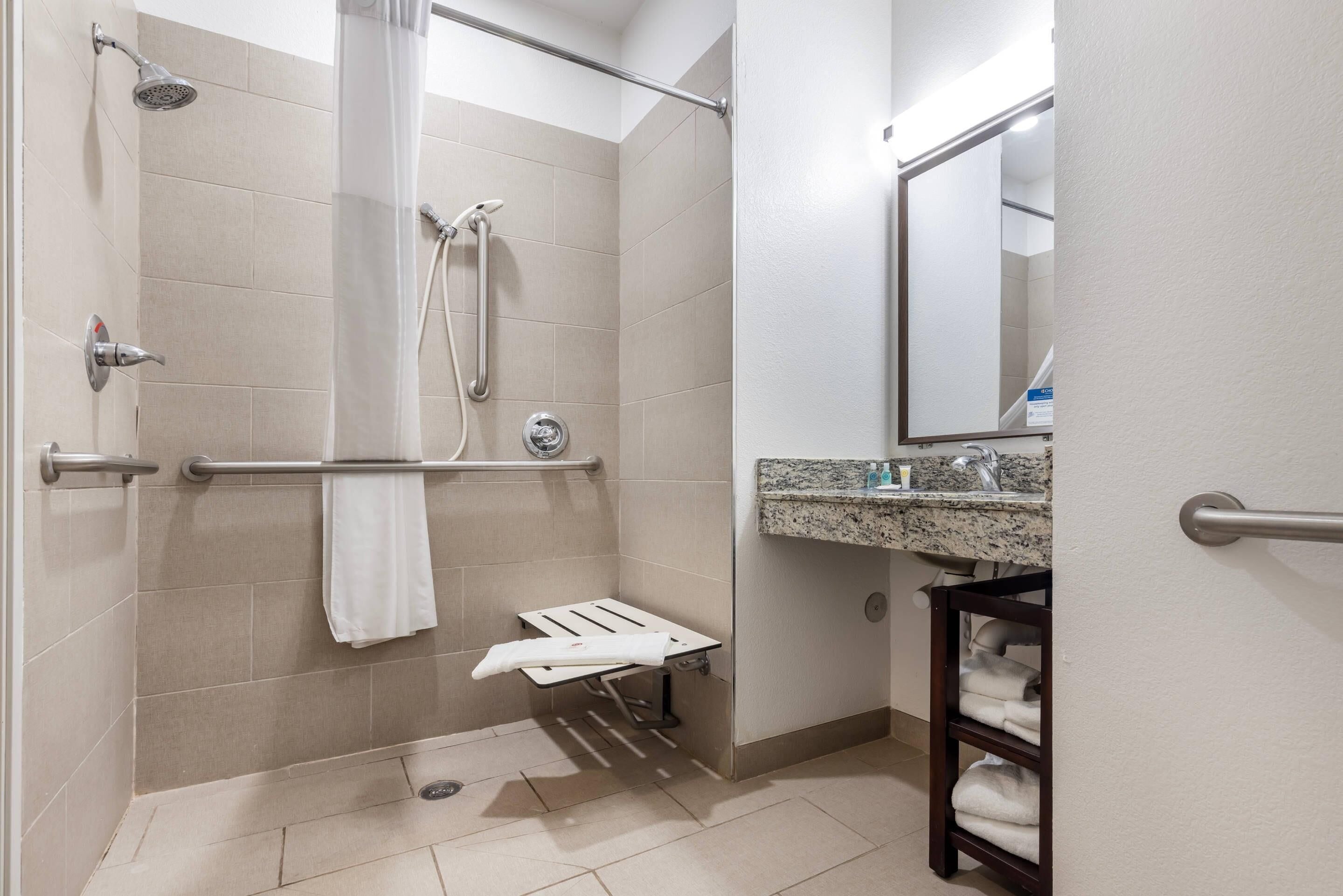 Un baño con ducha, barras de apoyo, toallero, lavabo con encimera de granito y espejo.