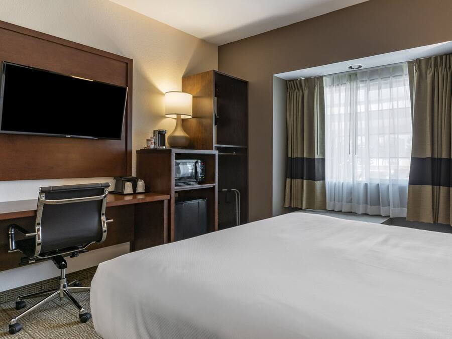 Habitación de hotel con una cama grande, un escritorio con silla, televisor de pantalla plana, microondas, cafetera y ventana con cortinas.
