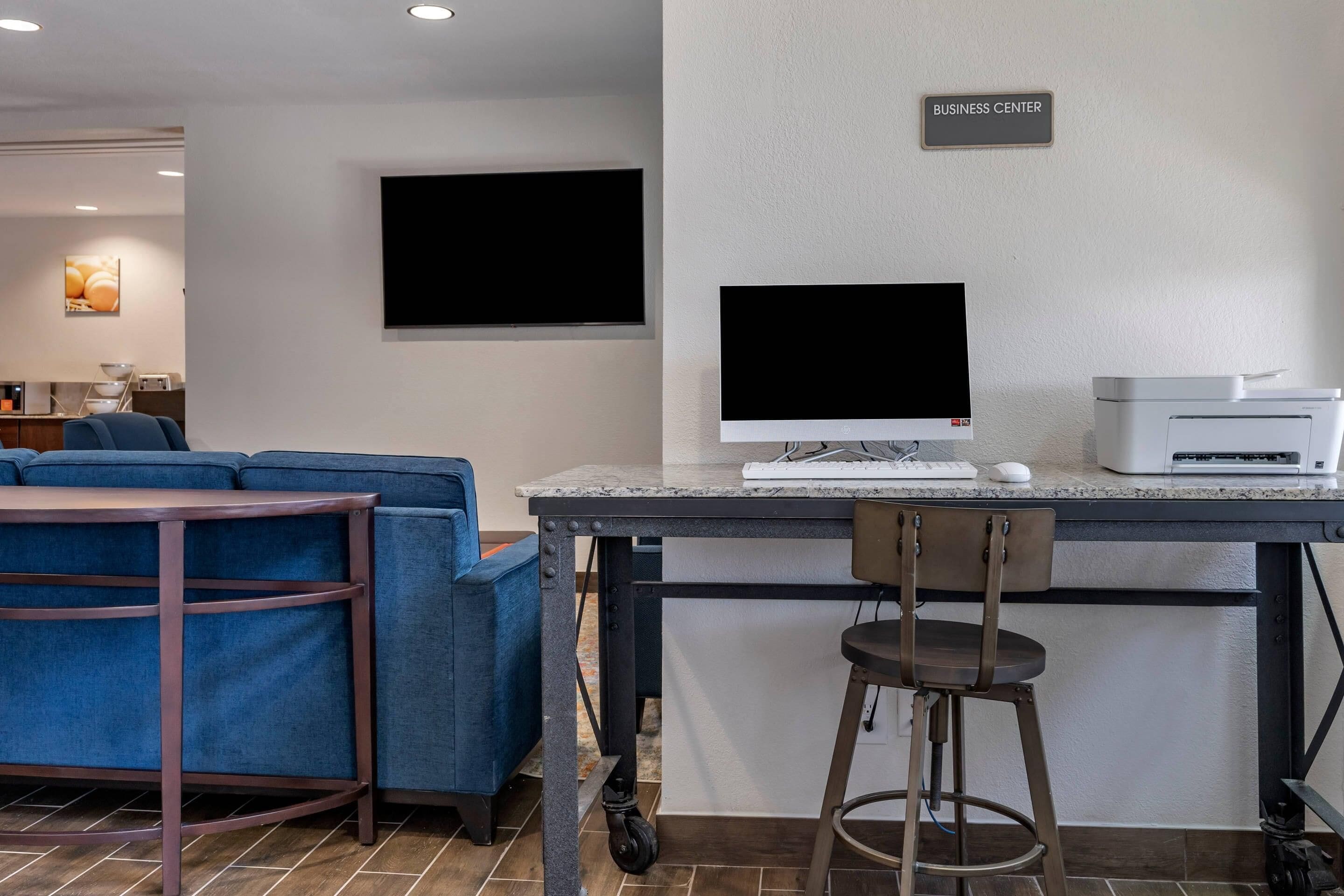 A modern workspace with a desk, computer, printer, and seating area.