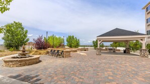 Un espace patio agrémenté d’une fontaine en pierre, de sièges d’extérieur et d’un espace barbecue couvert.