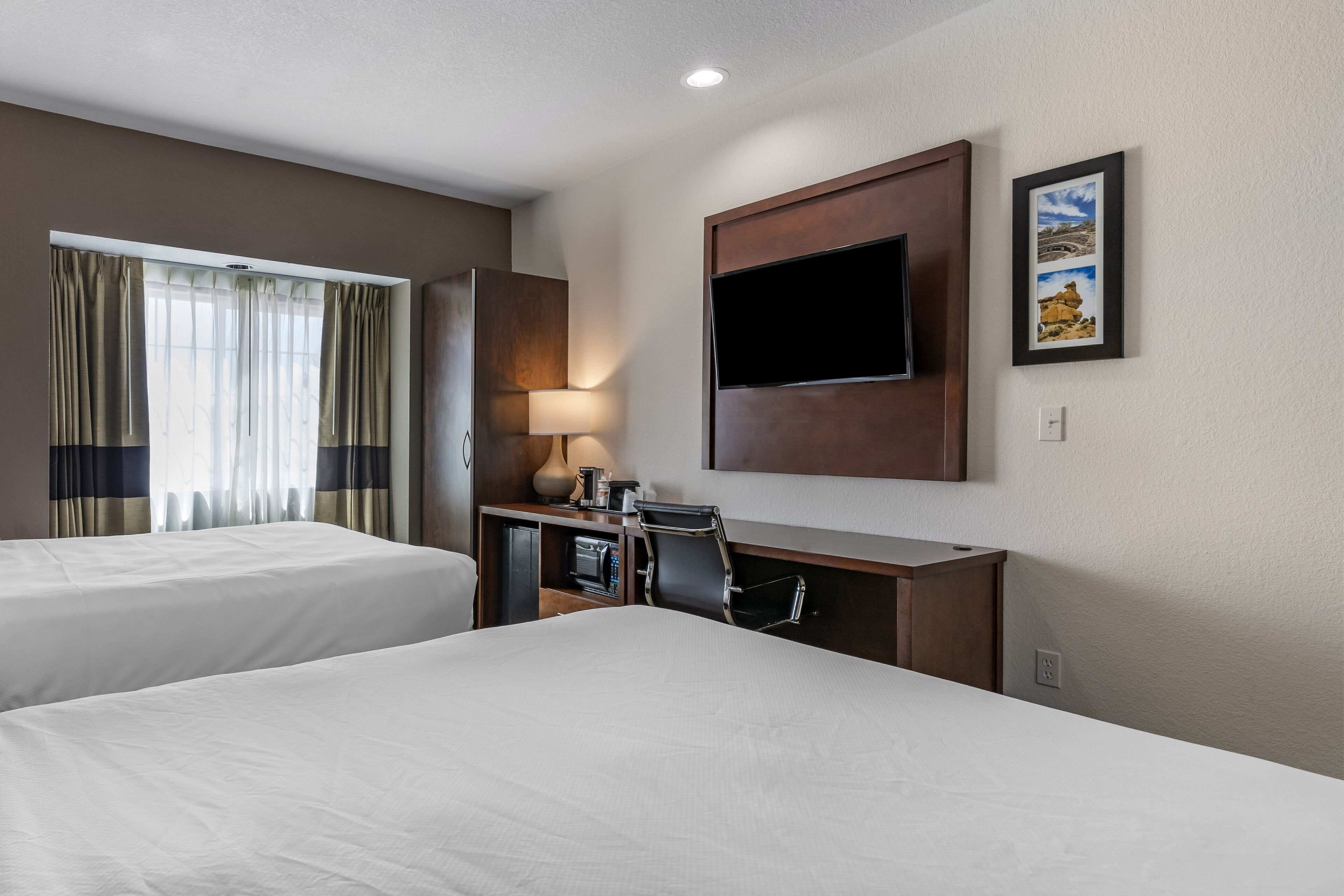 A hotel room with two beds, a desk with a lamp, a flat-screen TV, and a painting on the wall.