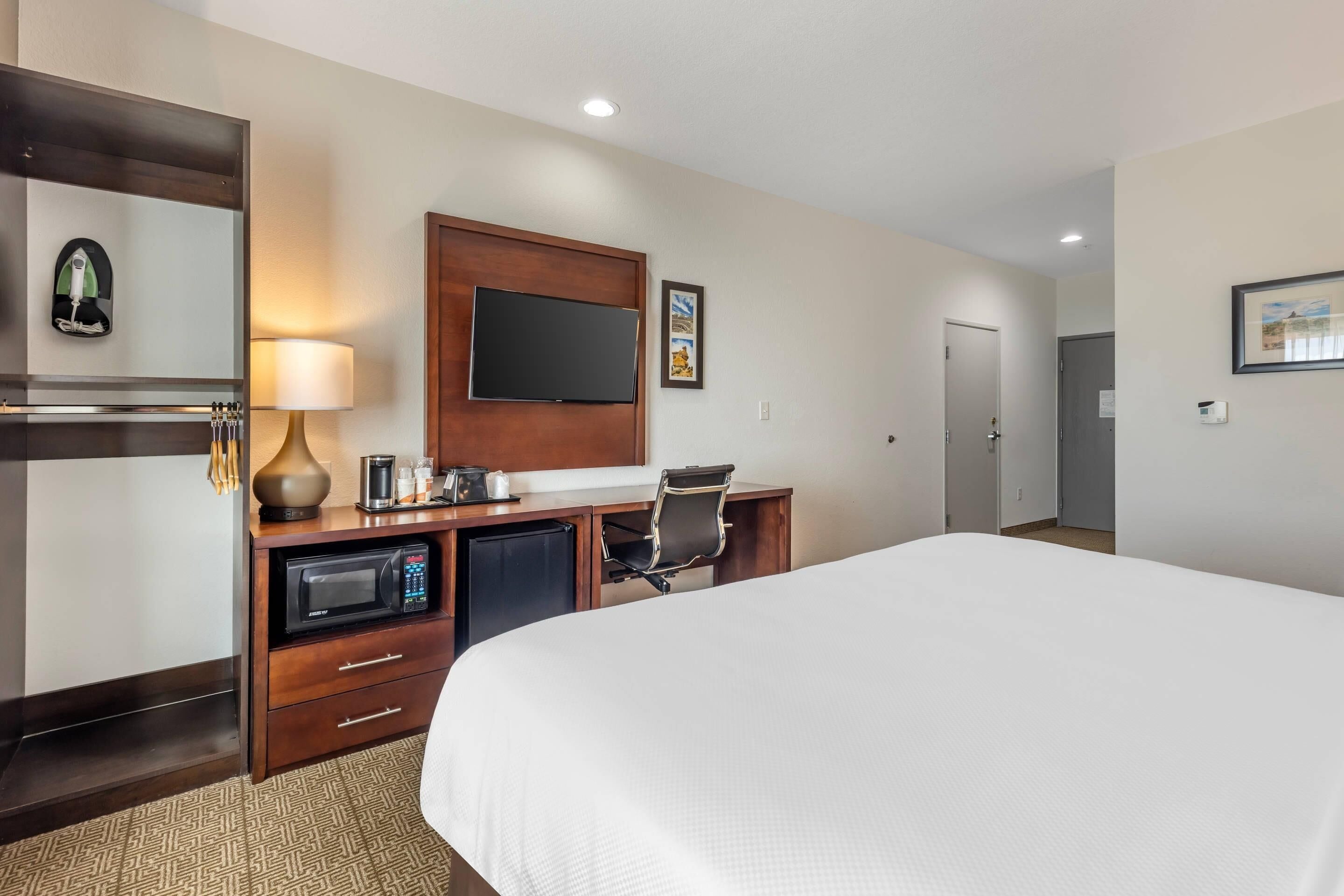 A hotel room with a large bed, a desk with a computer, a microwave, and a television.
