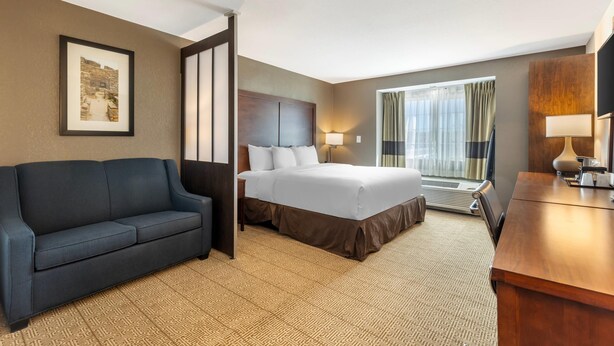 Une chambre d’hôtel avec un lit, un canapé, un bureau, une télévision et une fenêtre avec des rideaux.