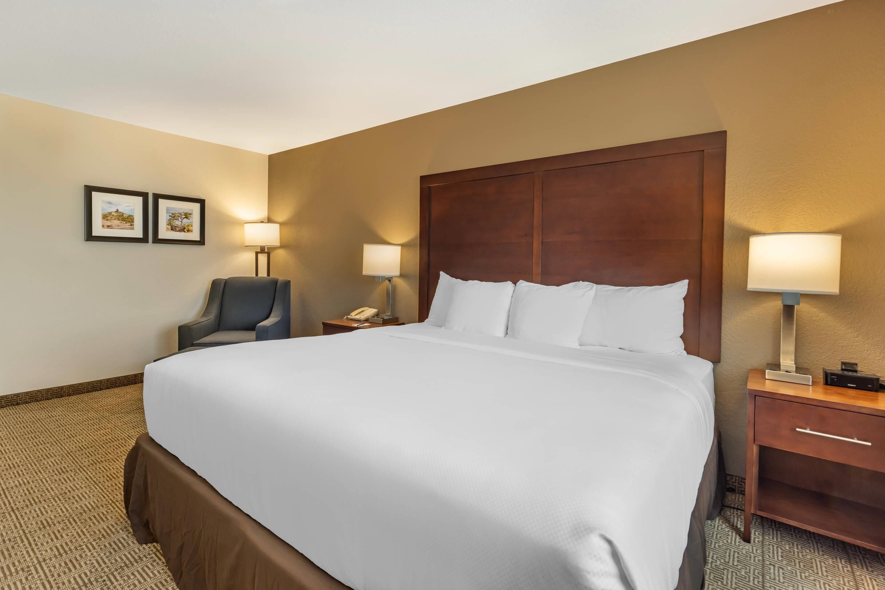 A hotel room with a large bed, two bedside tables with lamps, a chair, and two framed pictures on the wall.