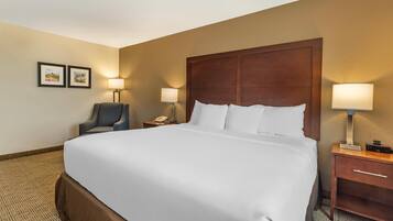A hotel room with a large bed, two bedside tables with lamps, a chair, and two framed pictures on the wall.